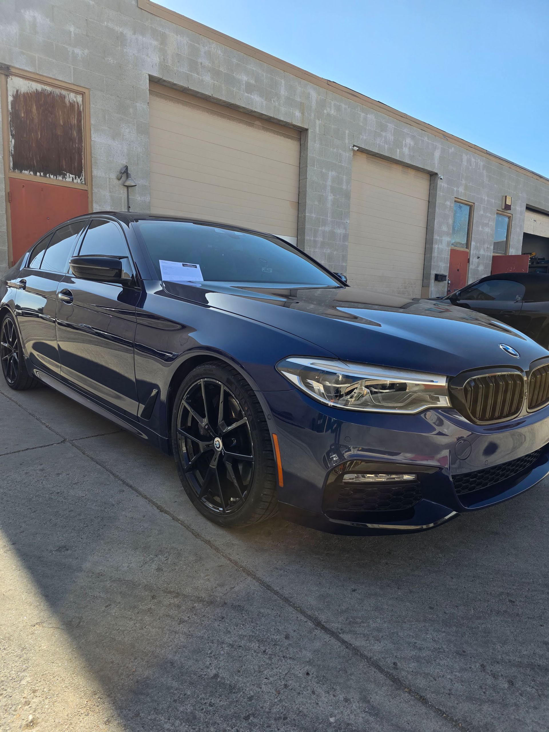 Dark blue BMW sedan parked by an industrial building with garage doors