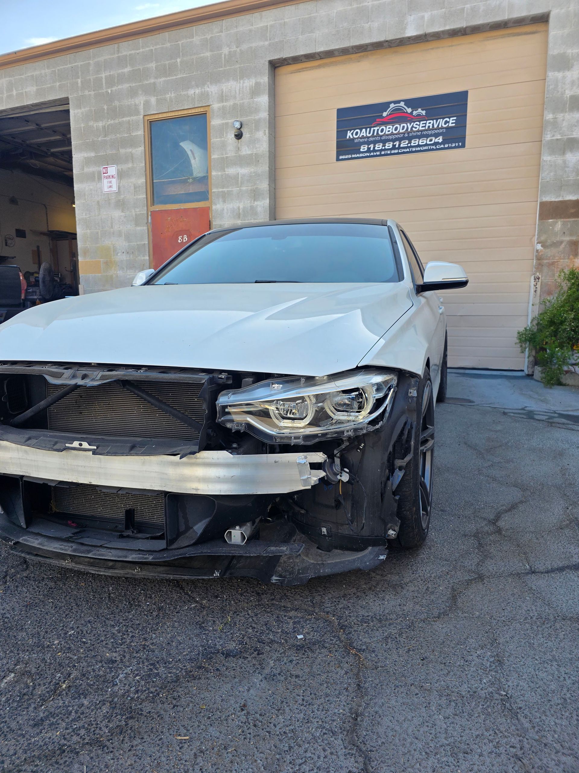 Damaged white car with a crumpled front end parked outside a brick building