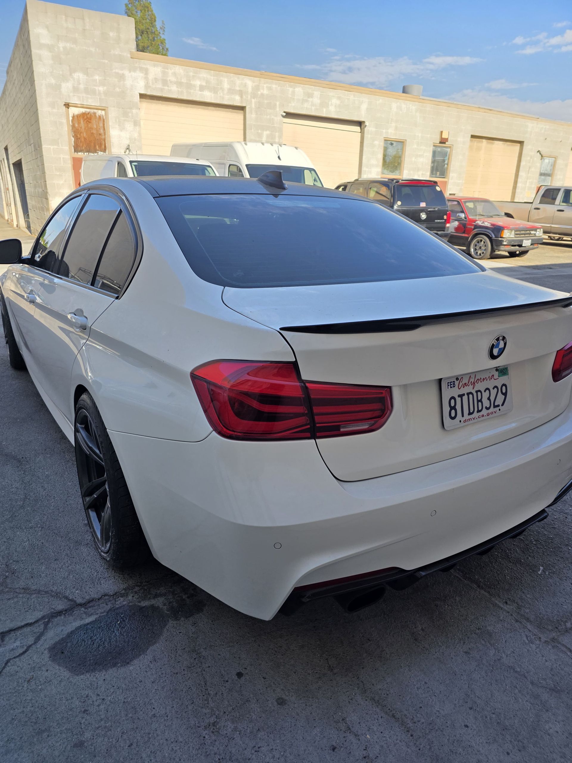 White BMW sedan parked outside an auto shop, rear view with visible license plate.