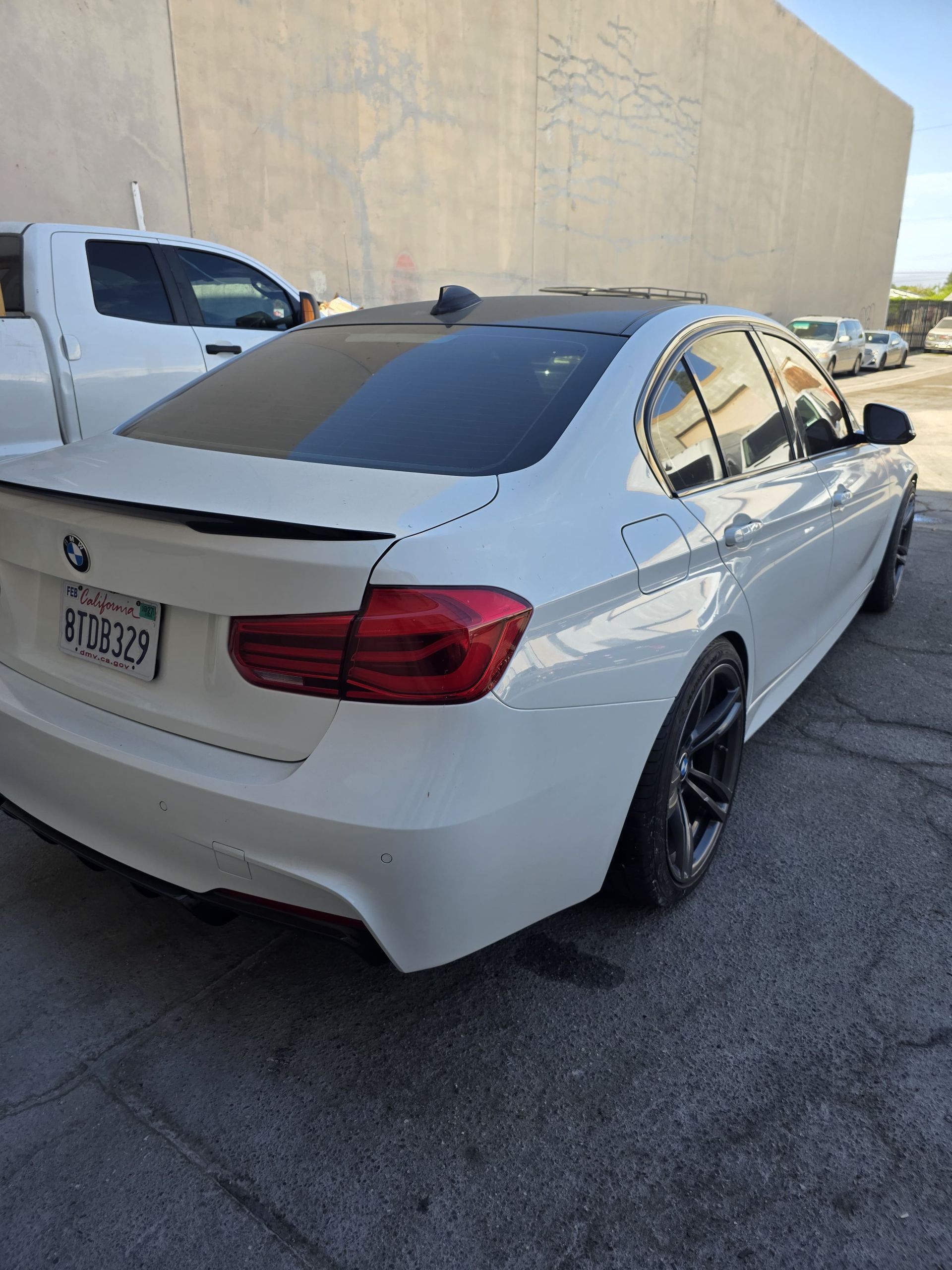 White BMW sedan parked beside a beige wall in a parking lot, rear three-quarter view.