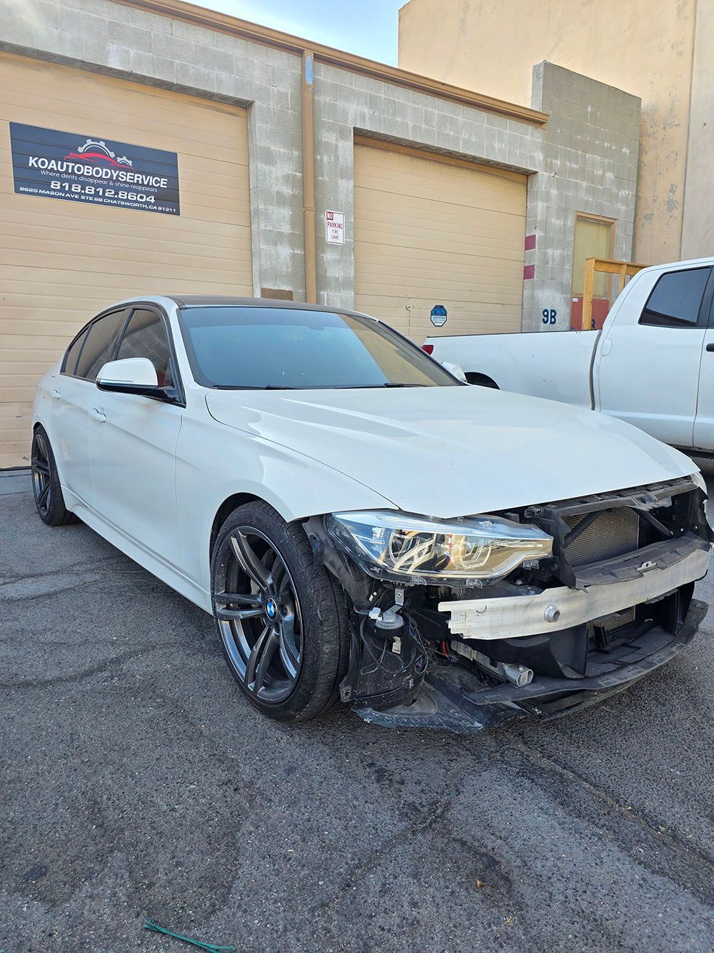 White sedan with front-end damage parked outside a beige industrial building.