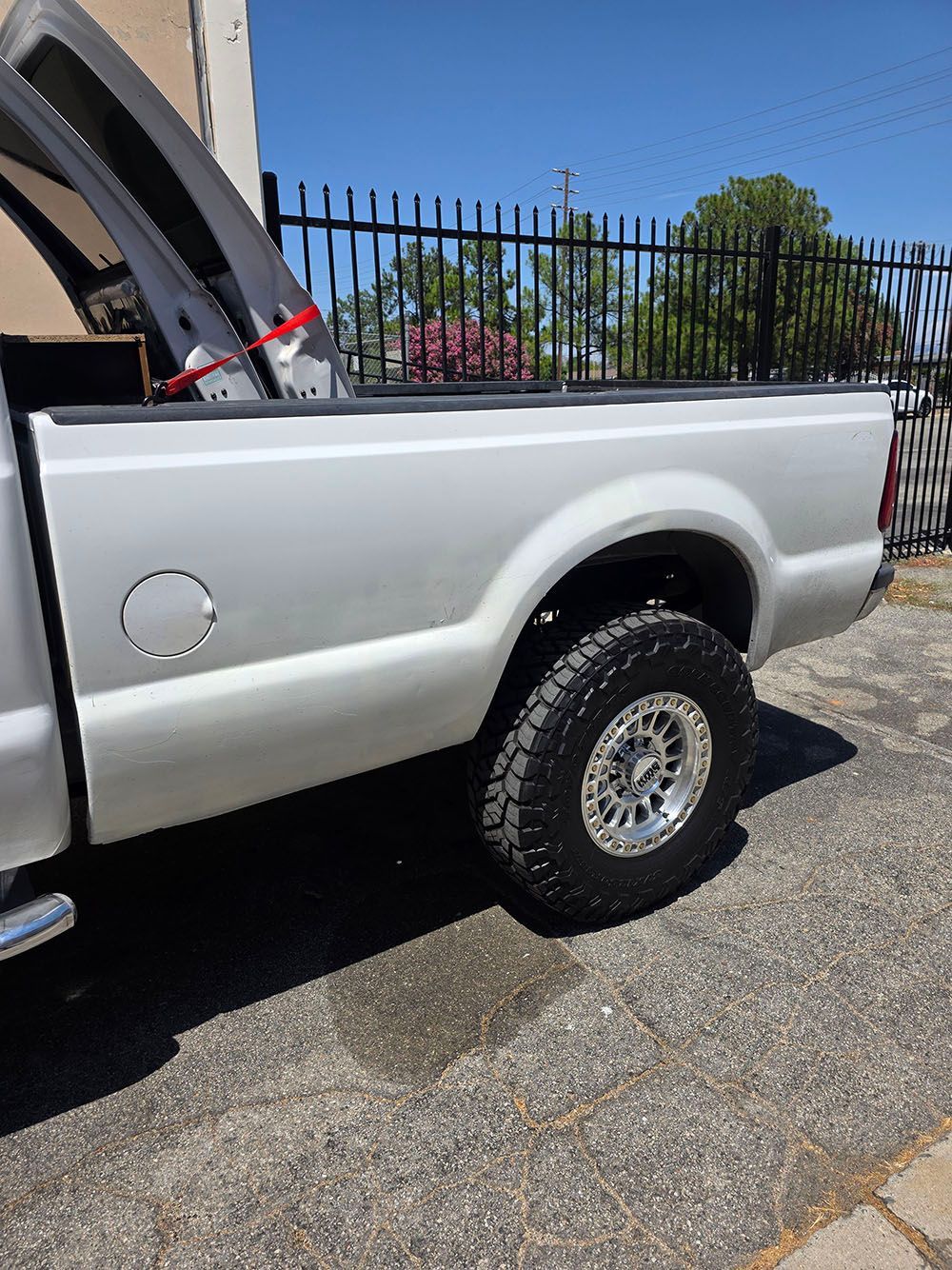 Silver pickup truck with raised bed cover, parked beside a fence in bright daylight