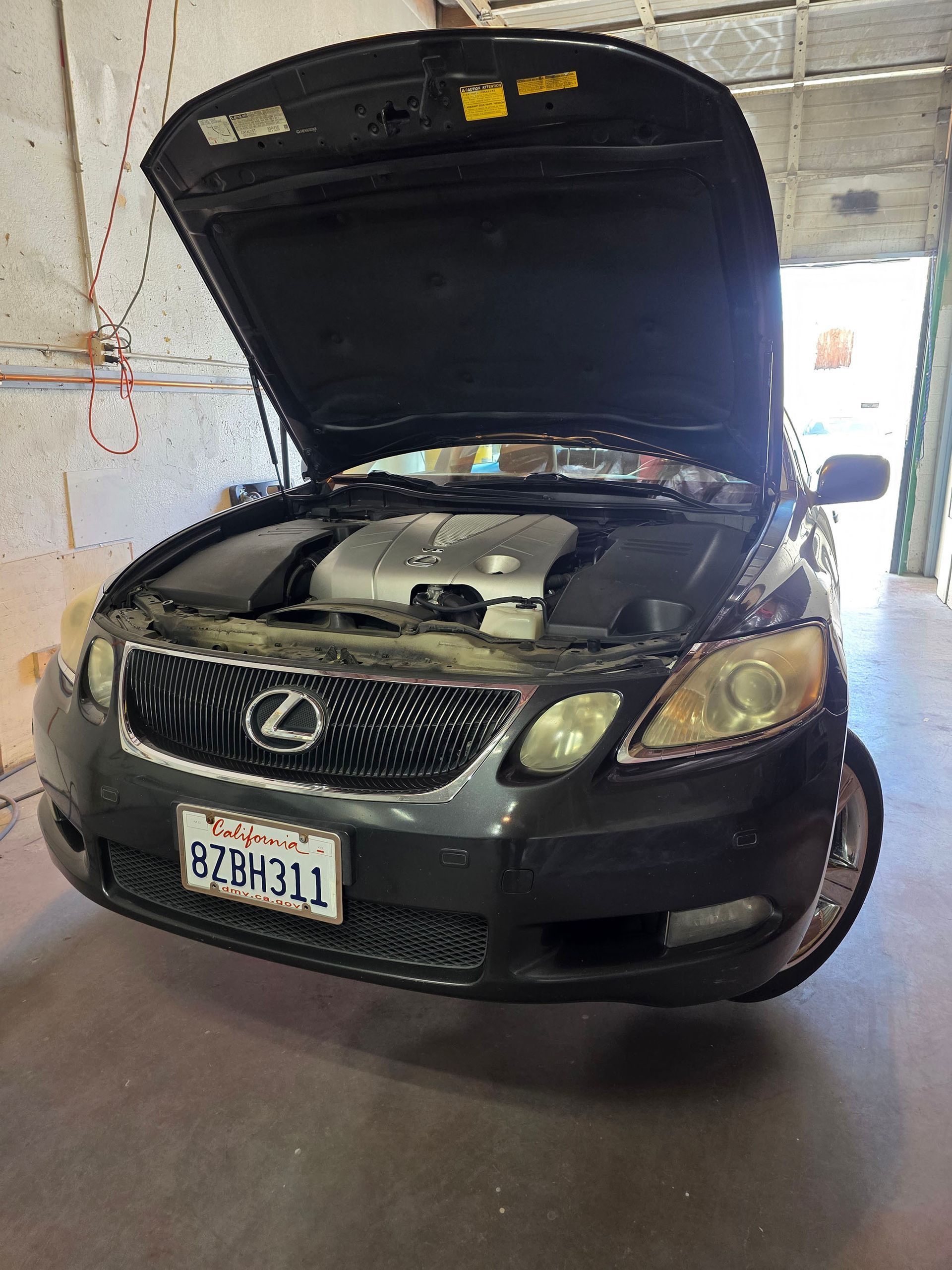 Black Lexus sedan in a garage with hood open, front view.