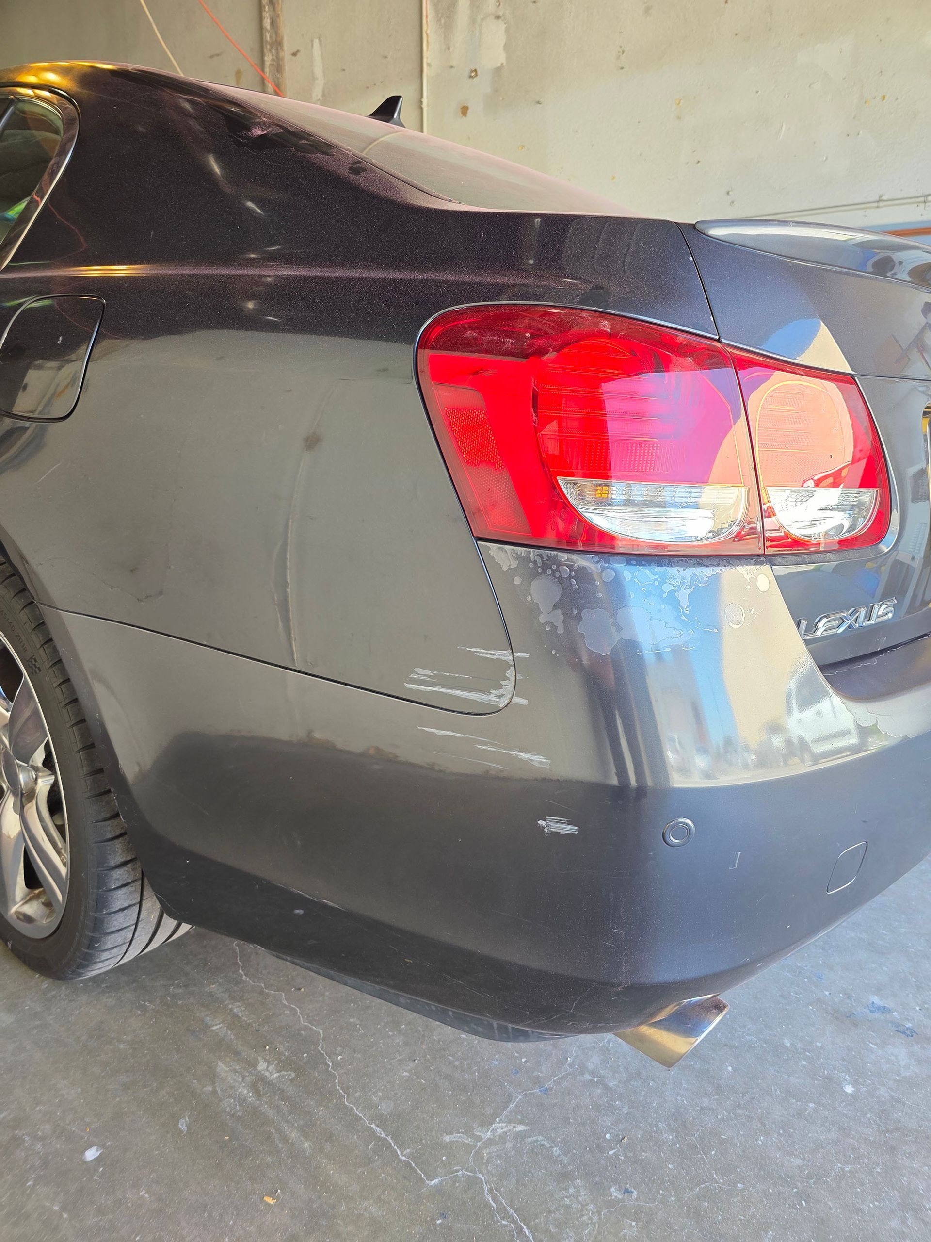 Rear-left view of a gray sedan in a garage, showing the taillight and rear bumper.