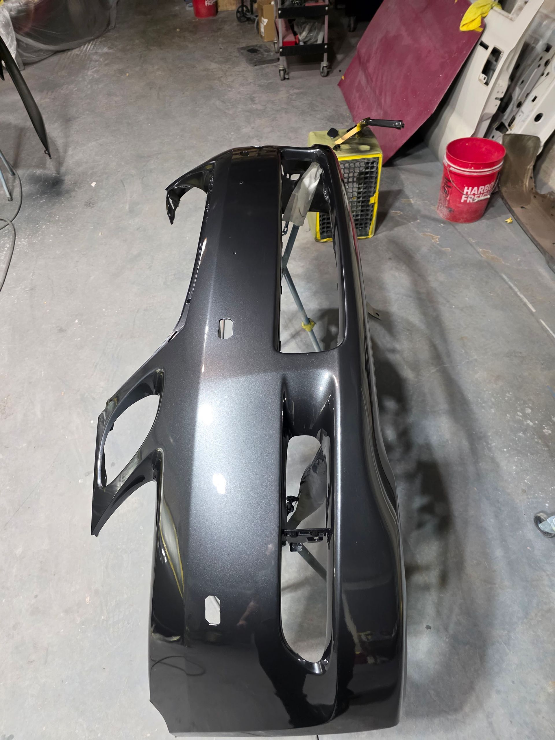 Black car bumper in a garage workshop, with red bucket and tools in the background