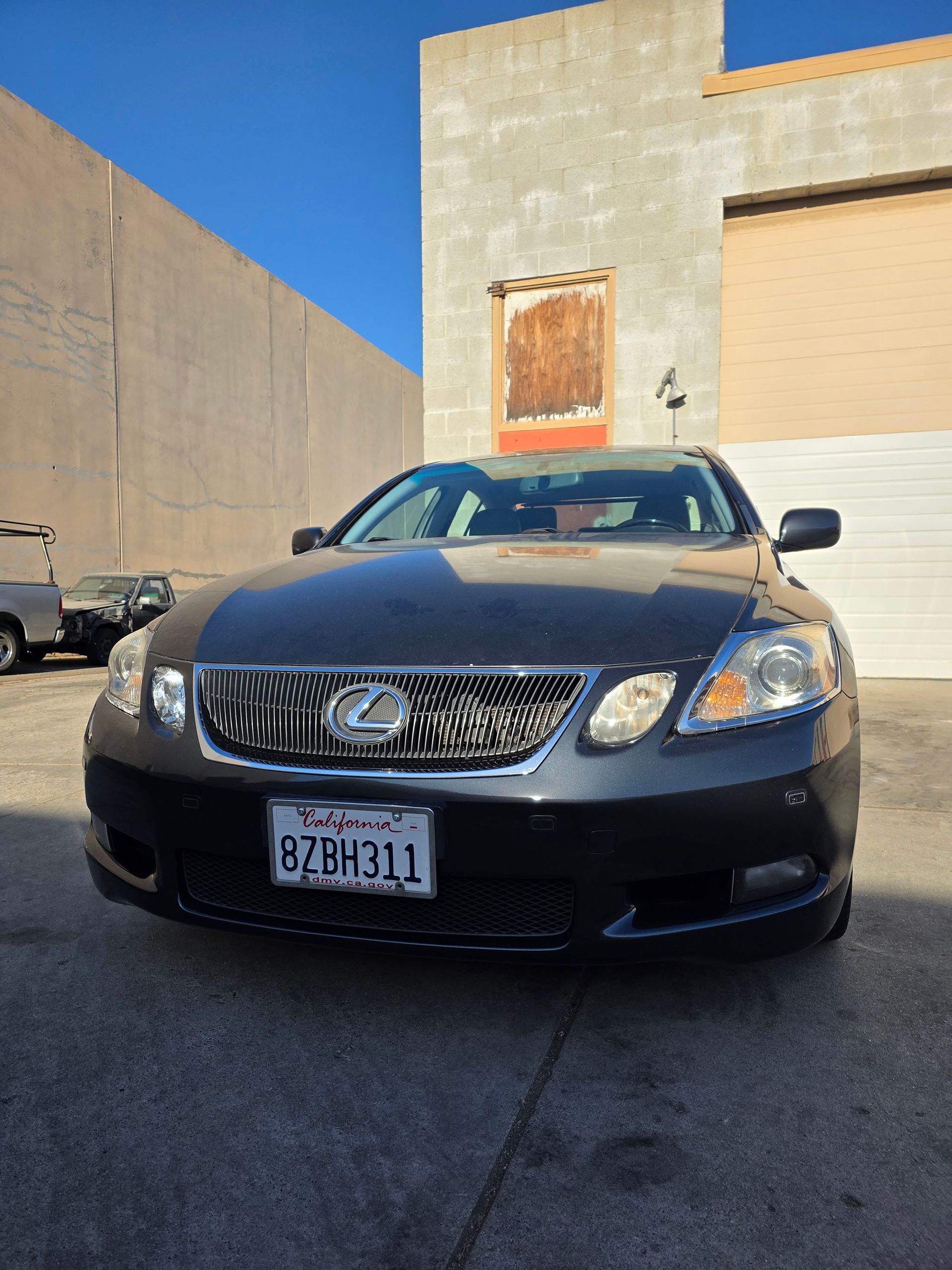 Black Lexus sedan parked in front of a building with a boarded window and beige walls