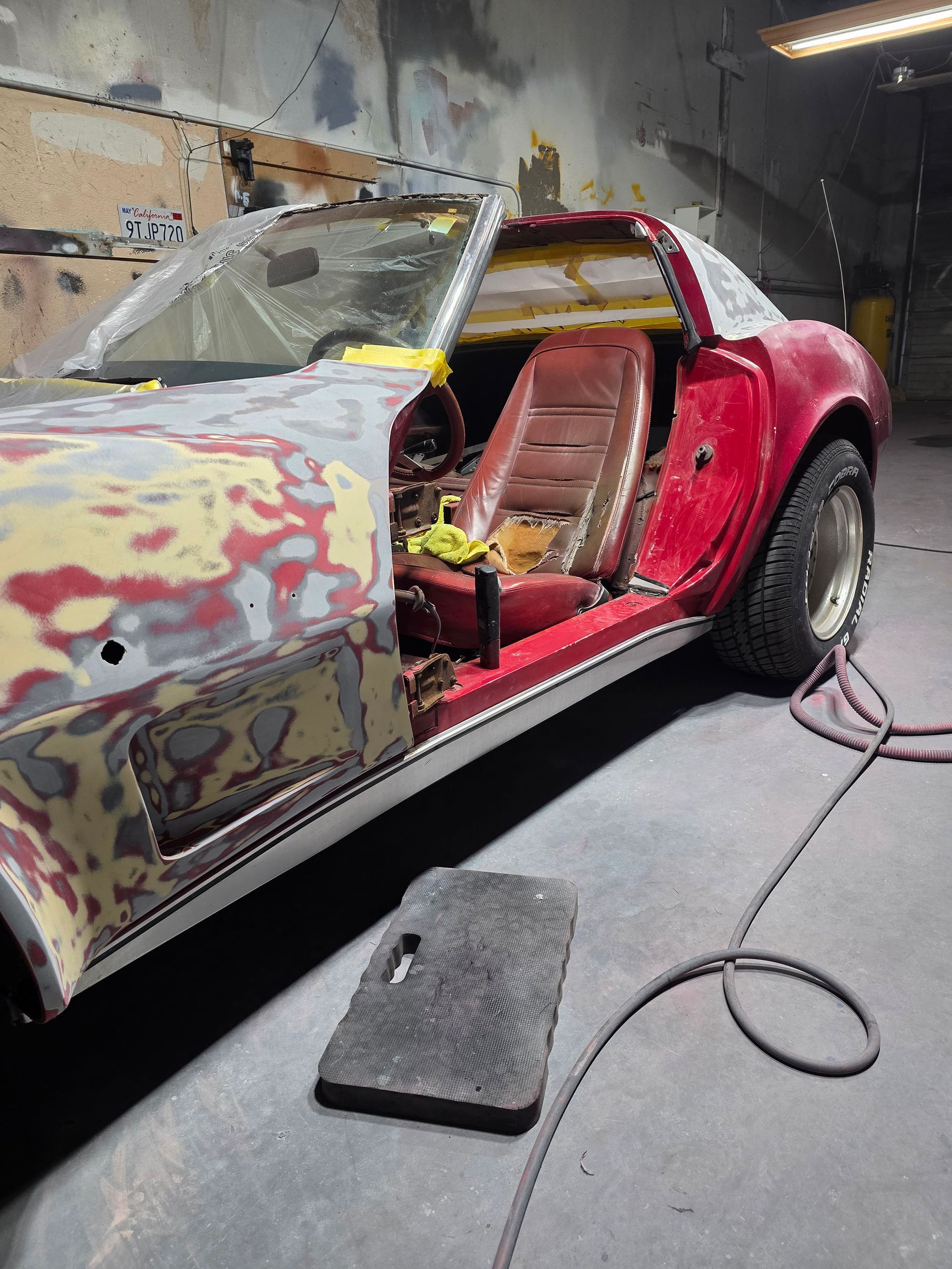 Partially restored red classic car in a workshop, with primer on the front and the door open.