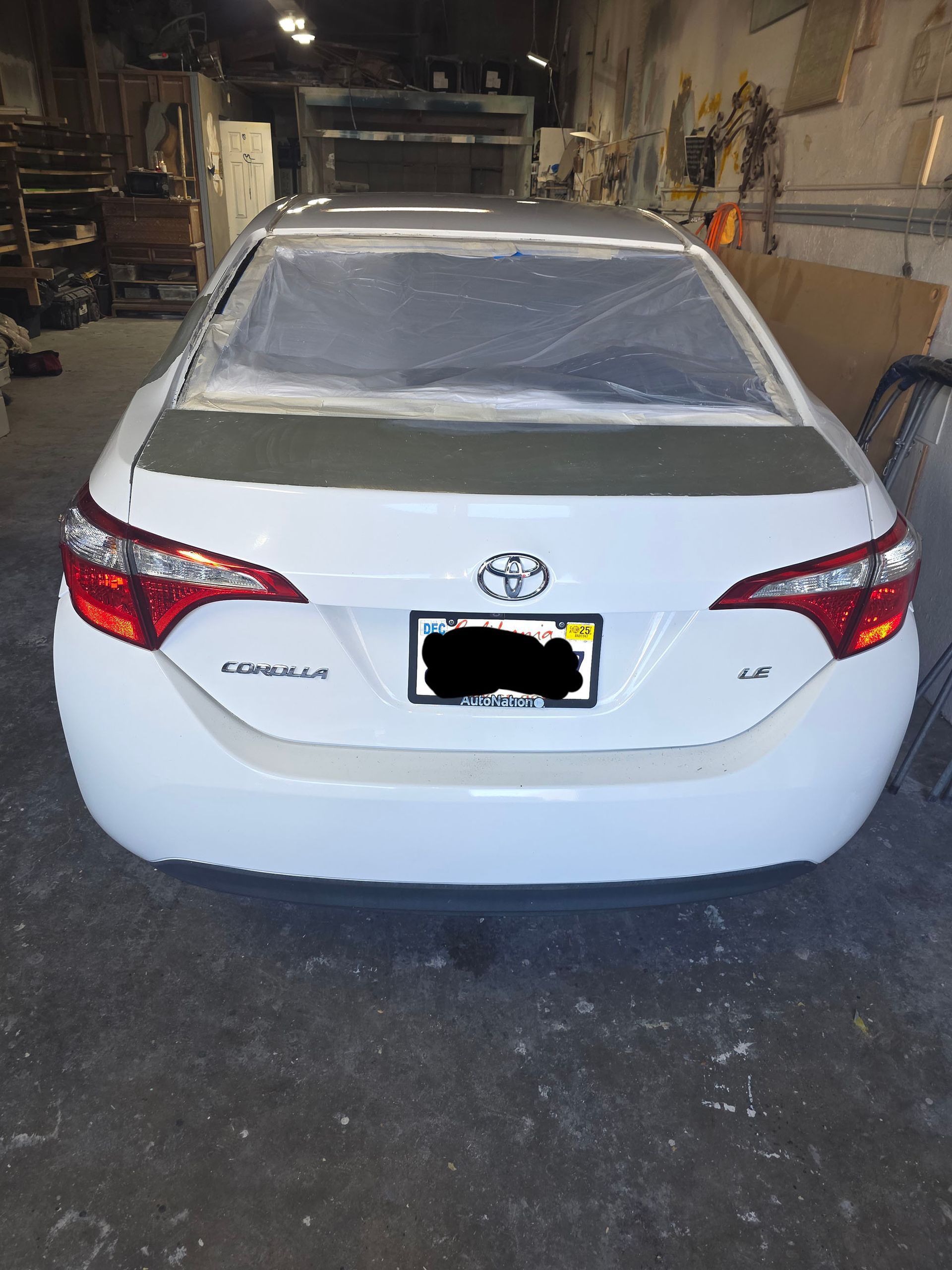 White Toyota sedan seen from the rear, parked inside a garage with a covered back window.