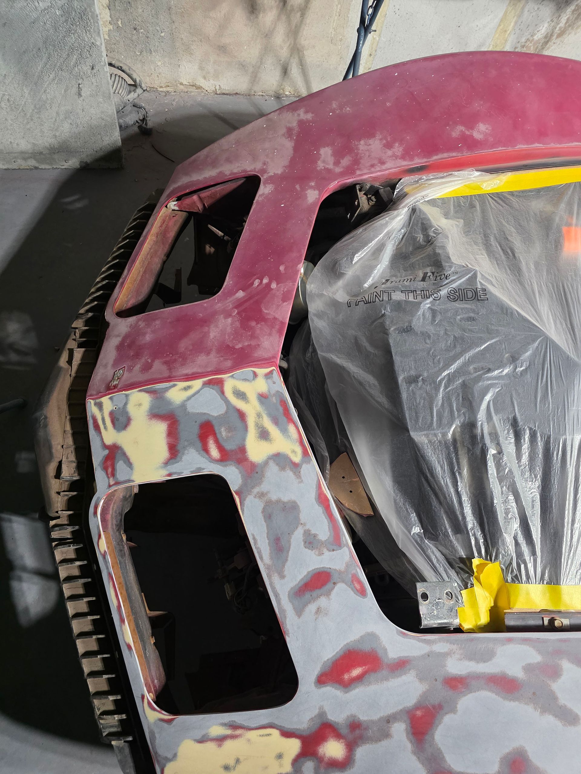 Scratched red car body panel with masked window and primer patches in a workshop