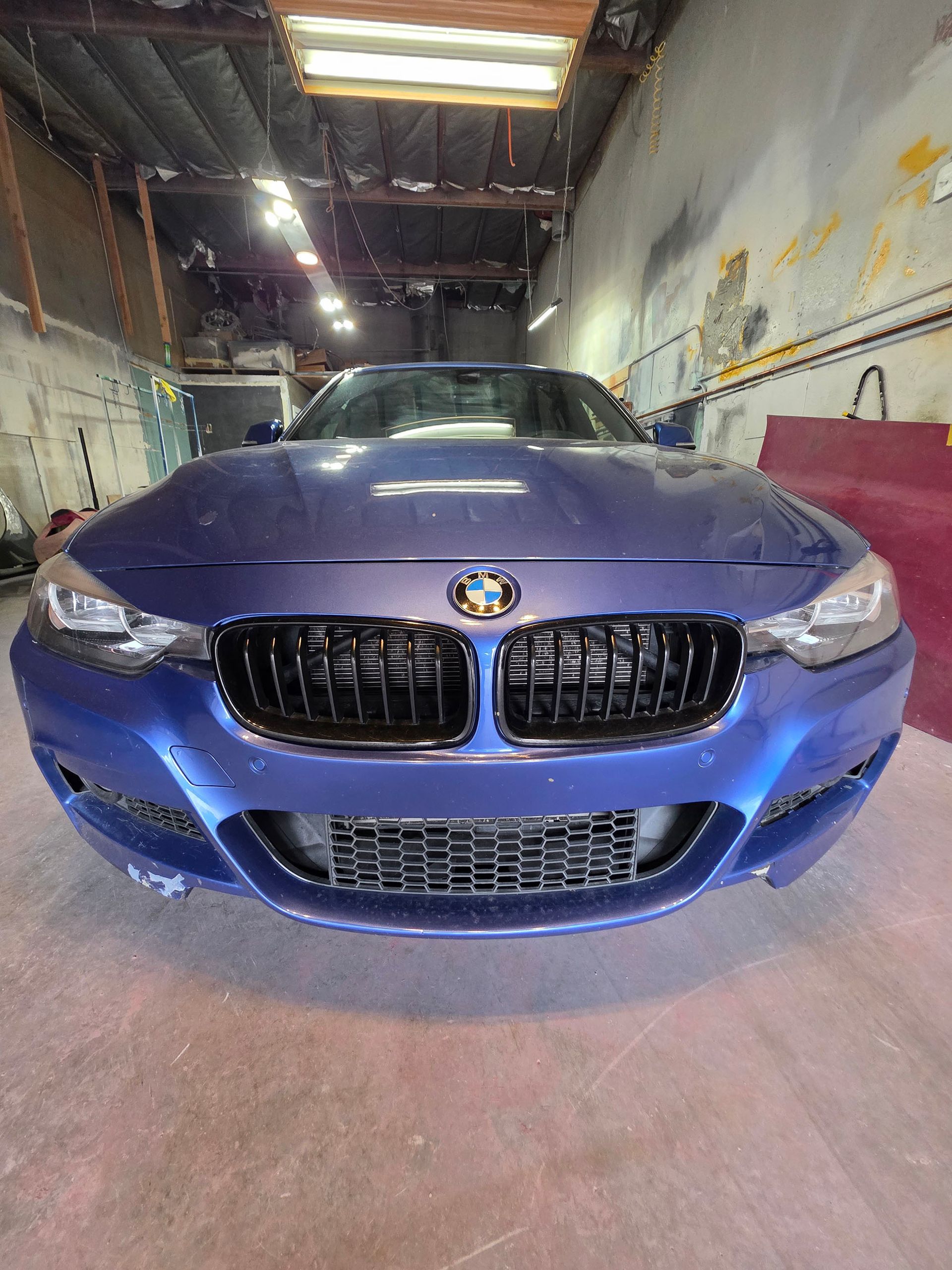 Blue BMW parked indoors in a garage, front view with grille and headlights visible