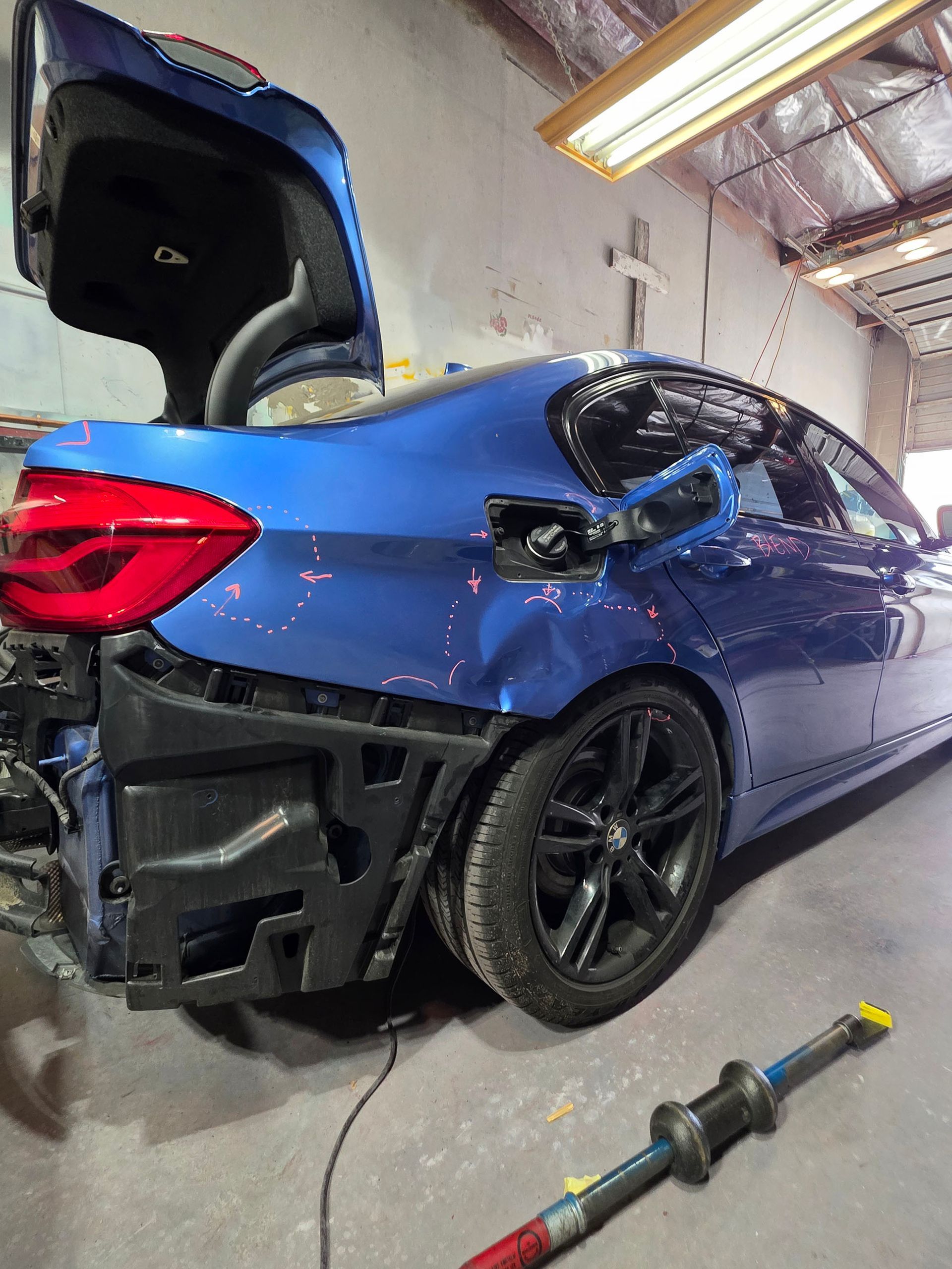 Blue car with rear hatch open and rear bumper removed in a workshop, with a power tool on the floor