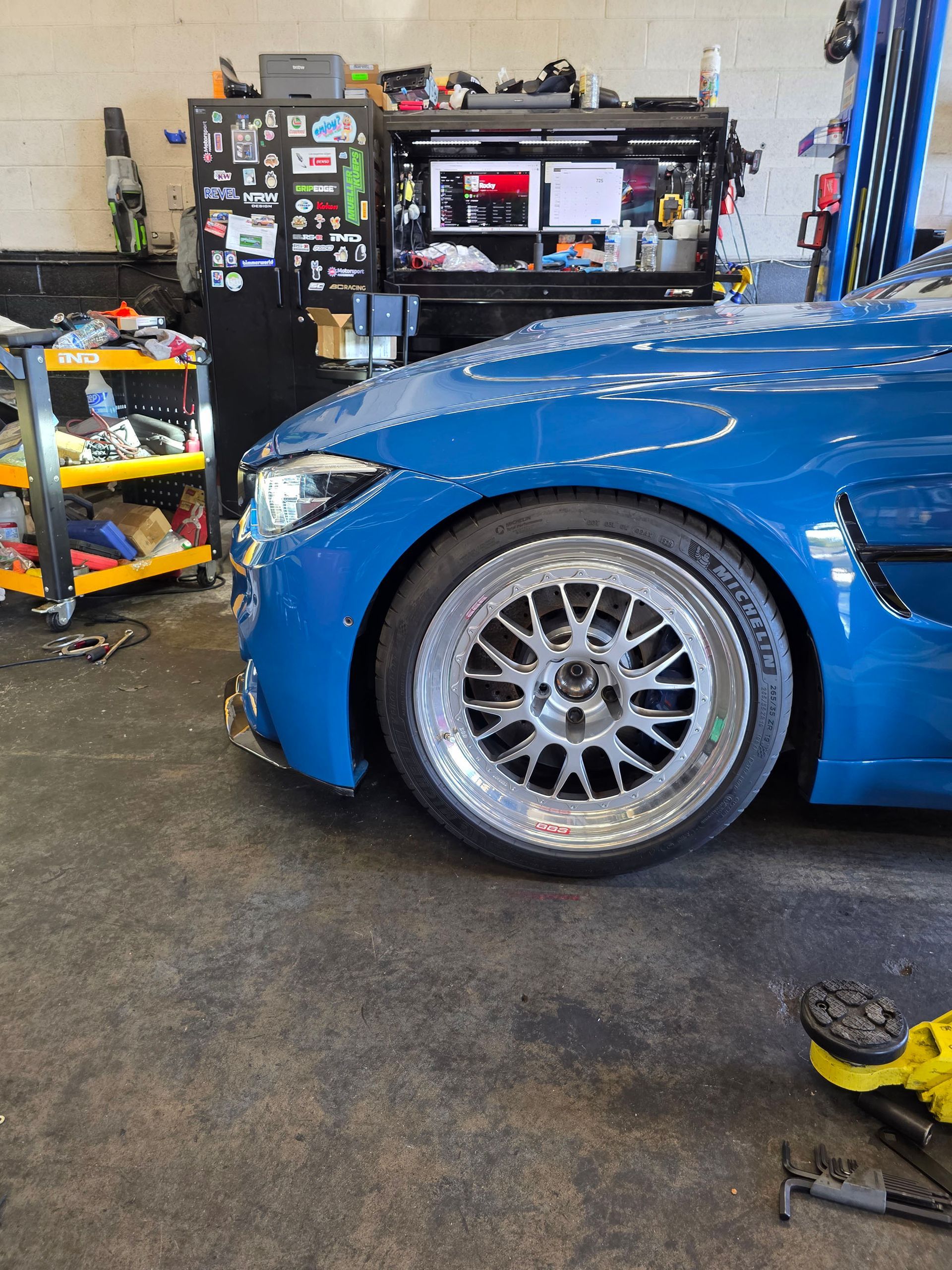 Blue car parked in a garage, showing a silver wheel and workbench in the background