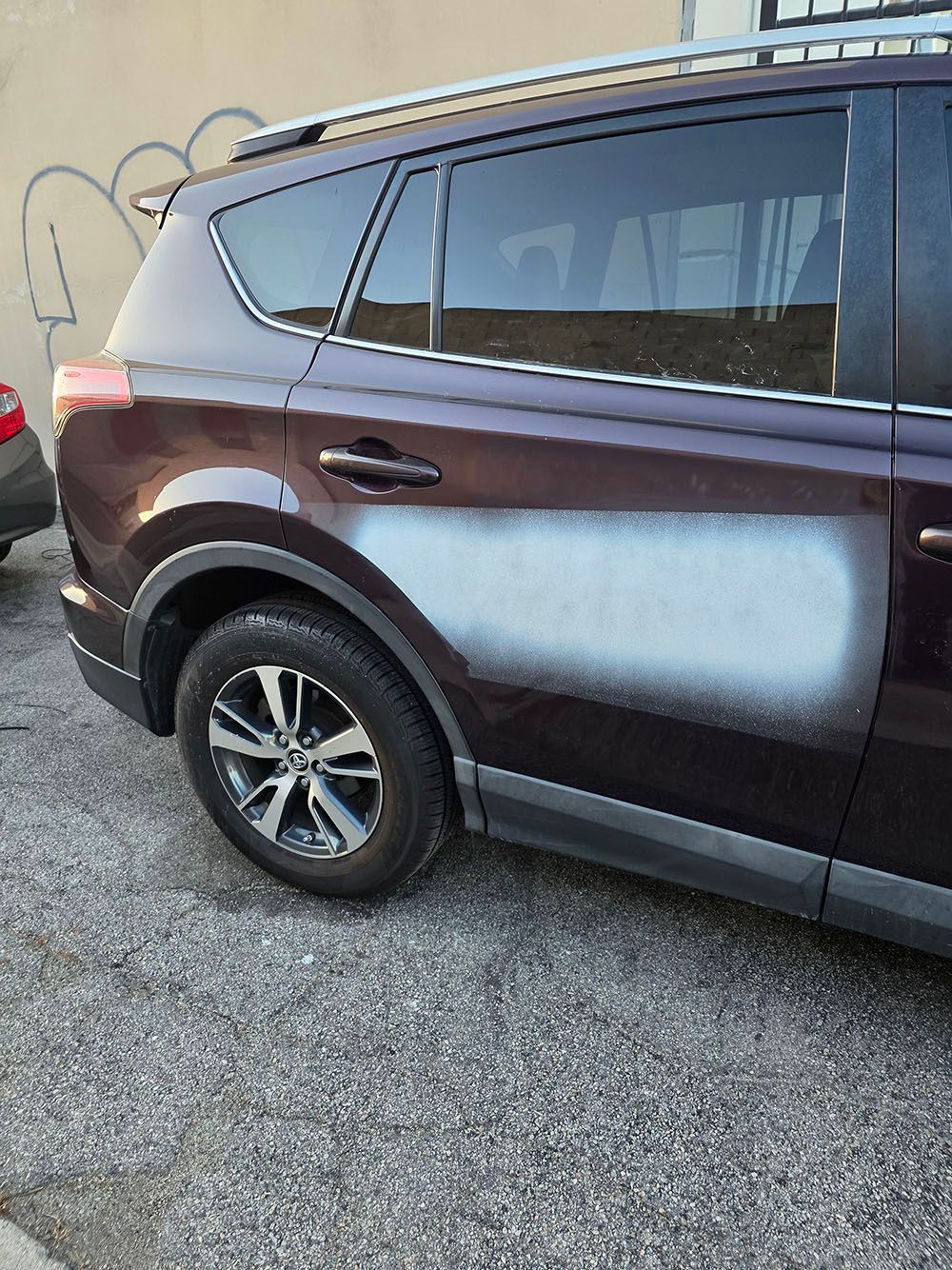 Dark maroon SUV parked on gravel beside a building, rear side view.