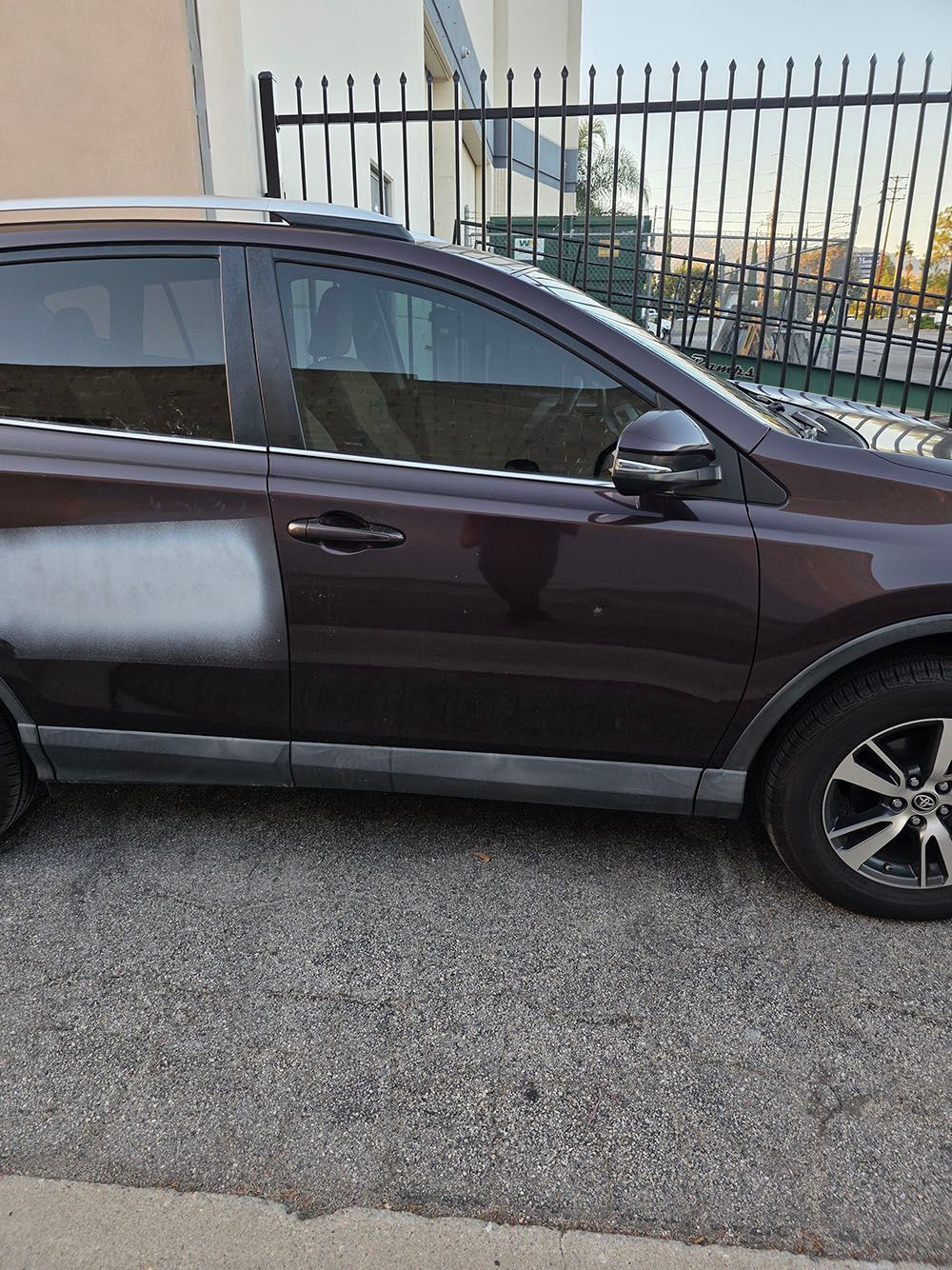 Dark maroon SUV parked beside a metal fence on a gravel roadside