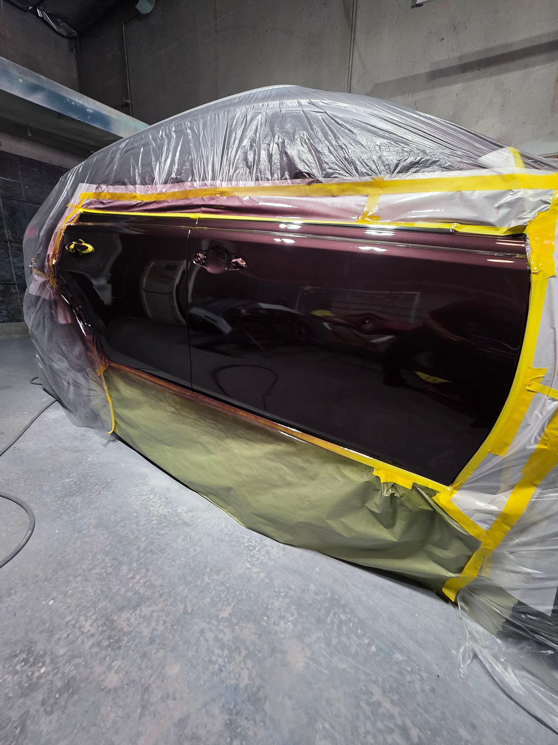 Car wrapped in plastic and yellow tape, parked indoors in a workshop or garage.