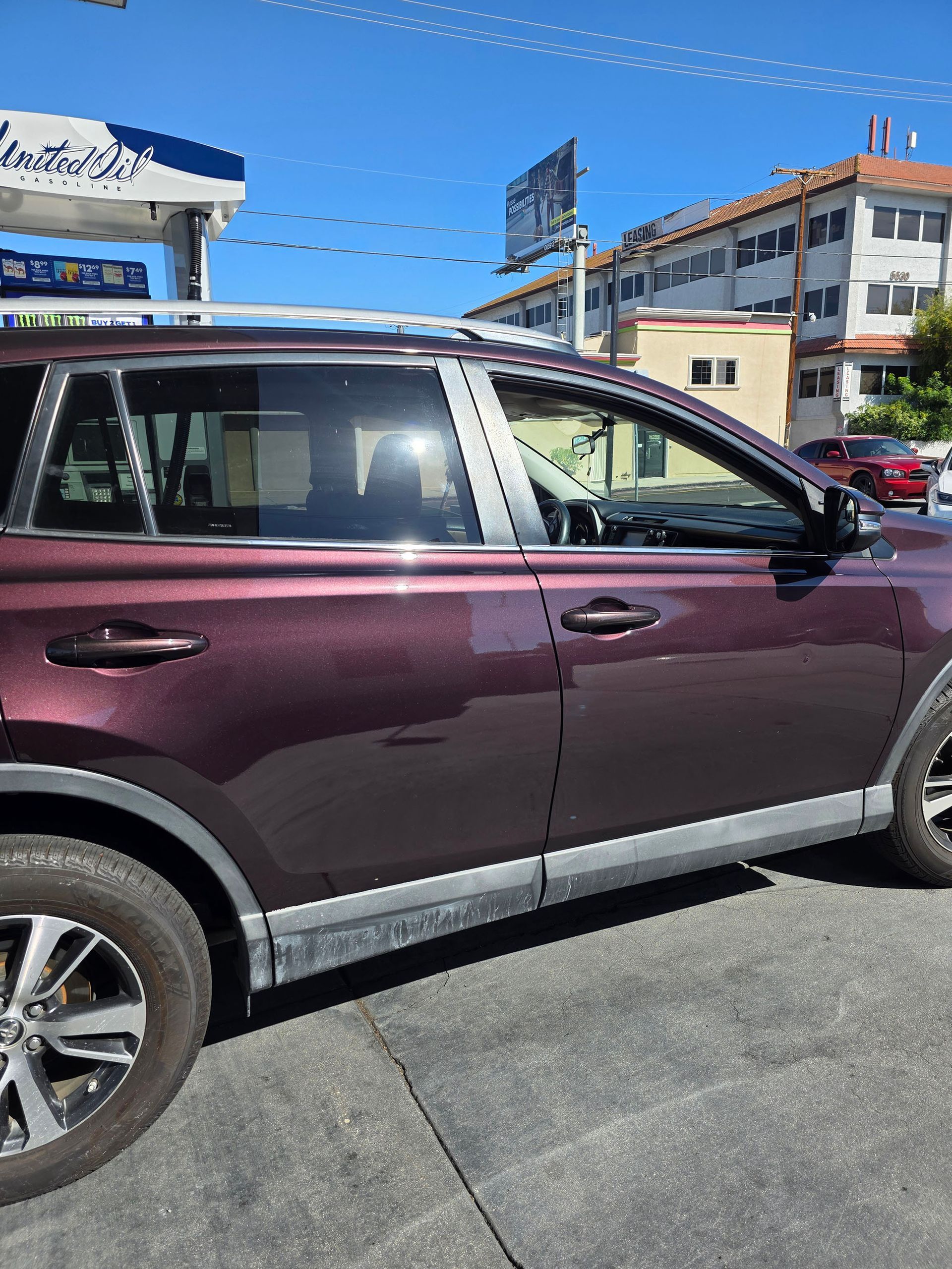 Maroon SUV parked on a sunny street with buildings and blue sky in the background