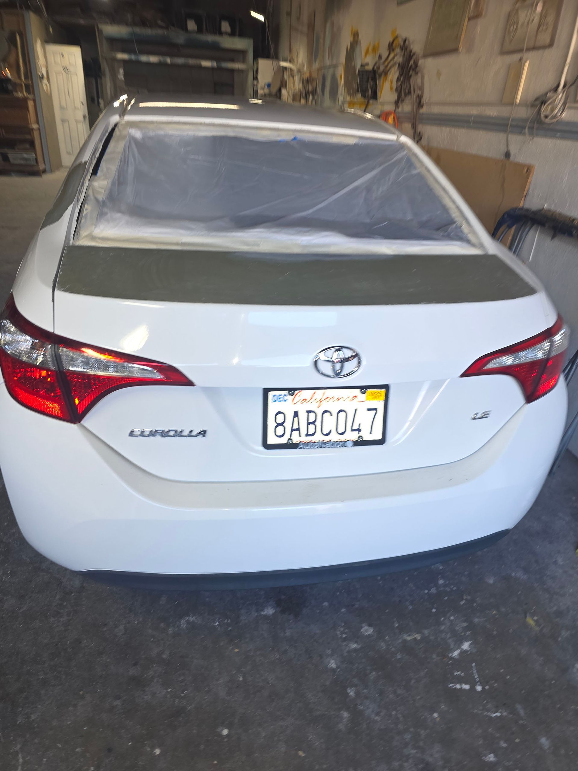 White Toyota sedan in a garage, rear view, with a covered rear window and license plate visible