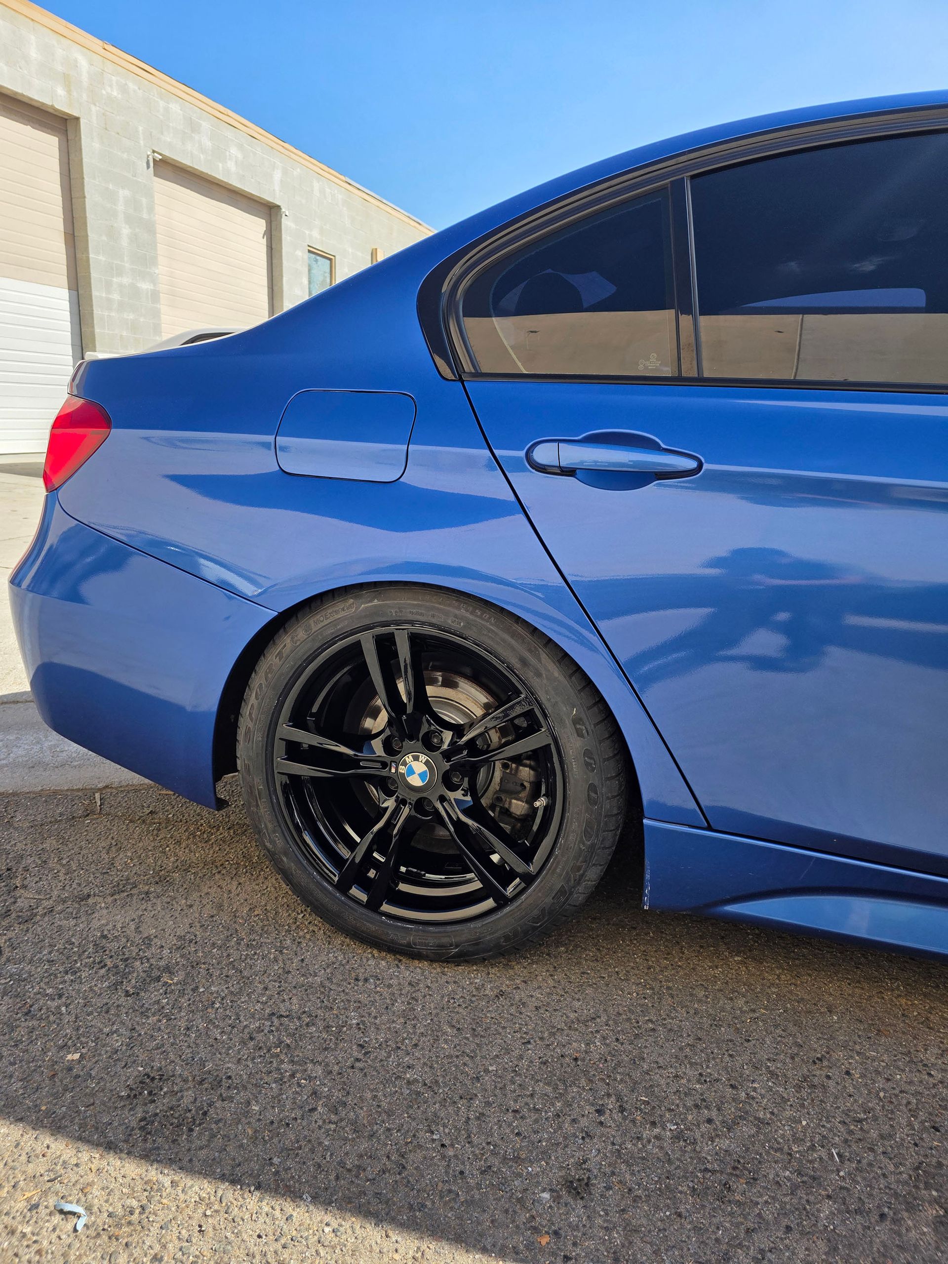 Blue sports sedan with black rims parked beside a building on pavement