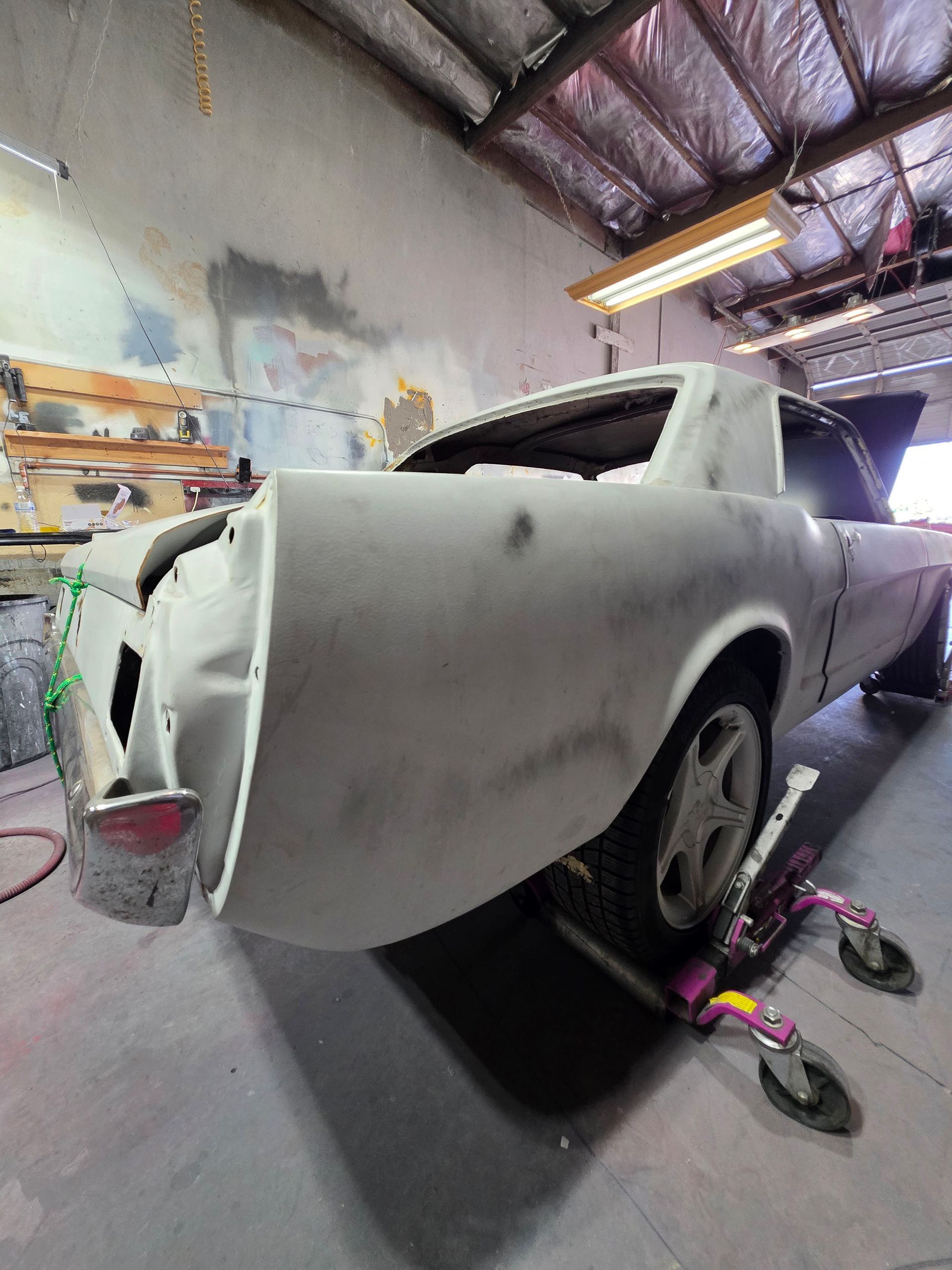Primer-gray classic car body in a workshop, partly masked and resting on stands during restoration.