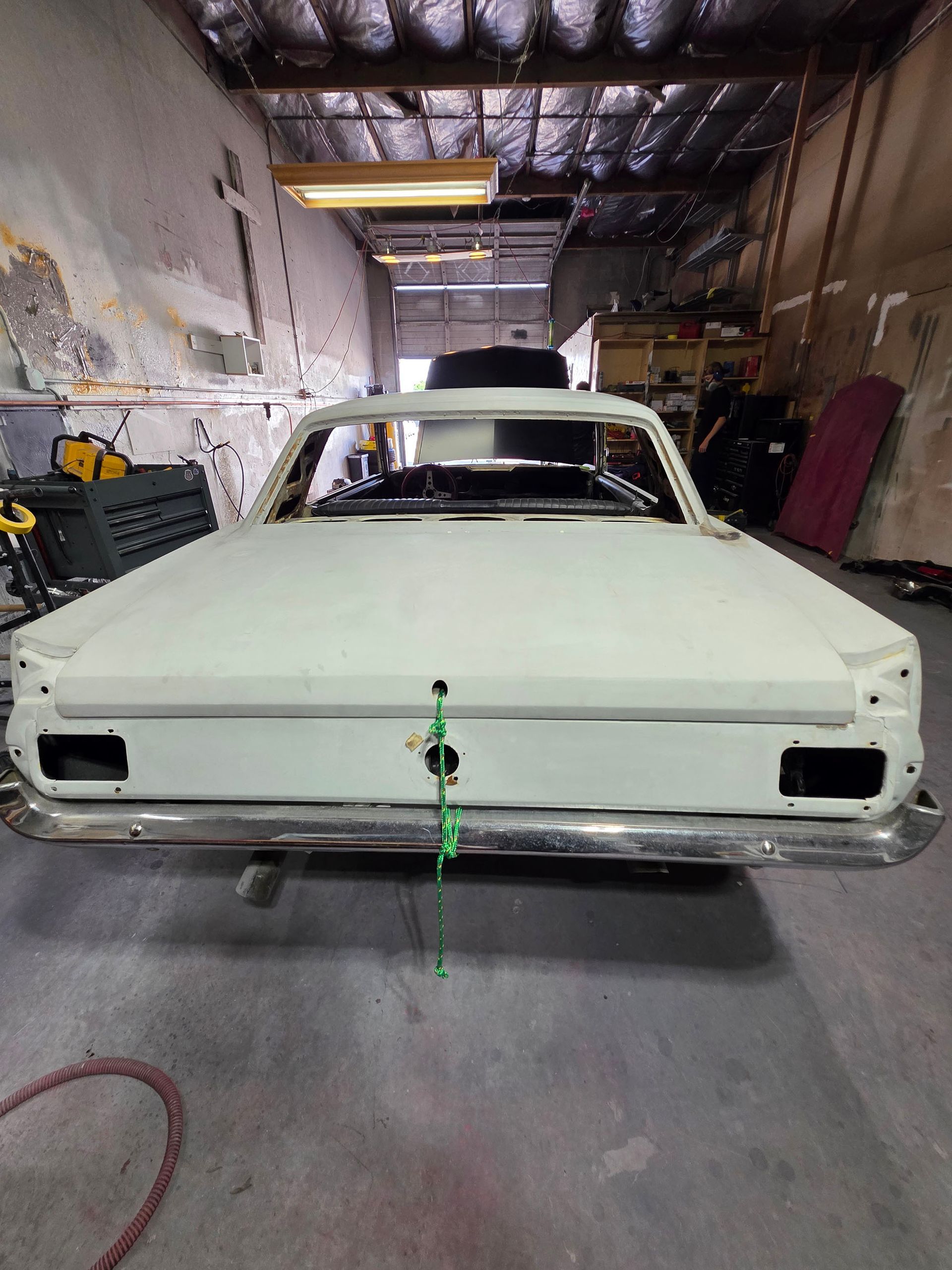 Primered classic car body in a garage with a green strap hanging from the front.