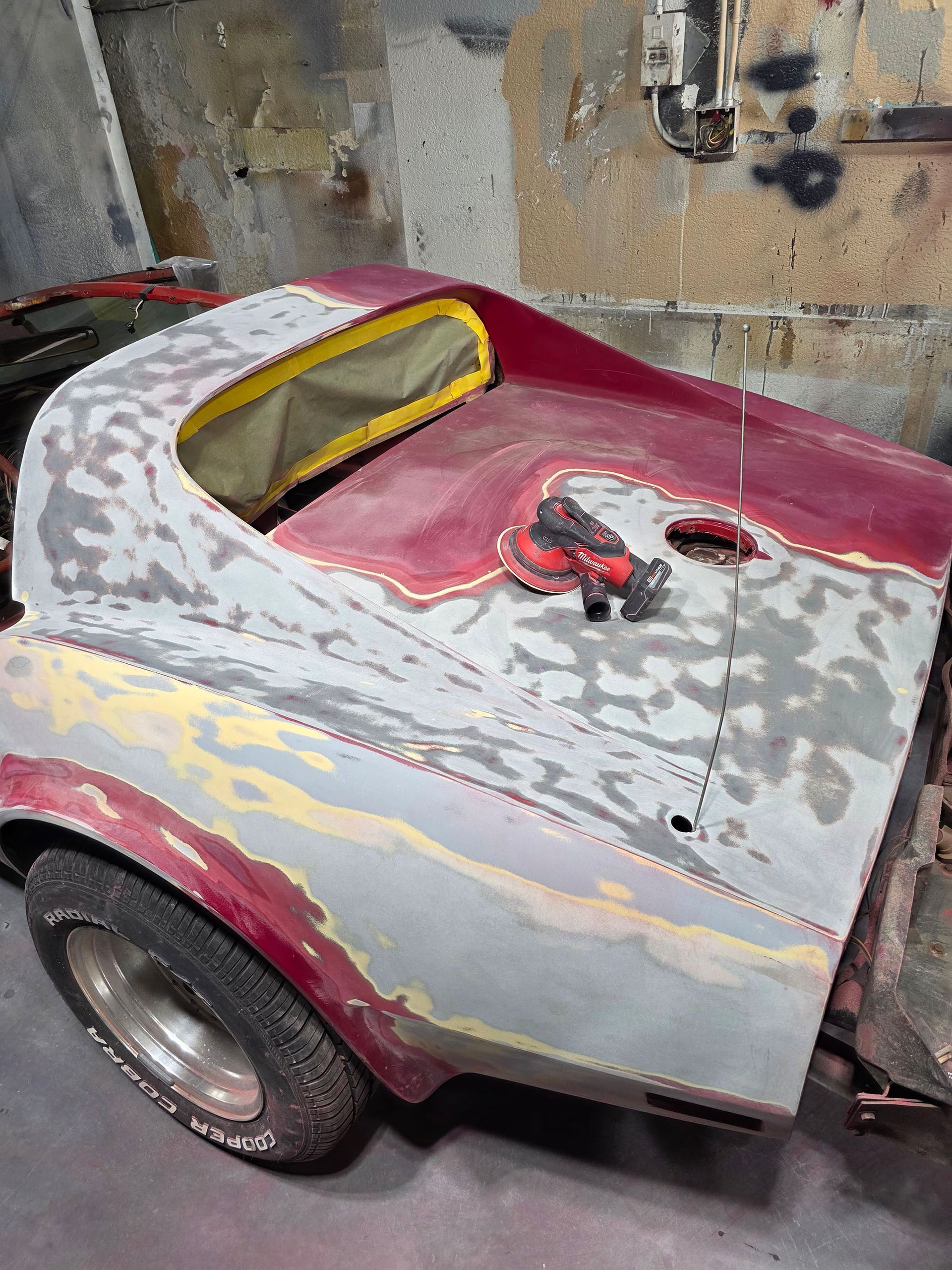 Customized pink-and-gray car body in a workshop, with tools on the rear deck and primer visible.