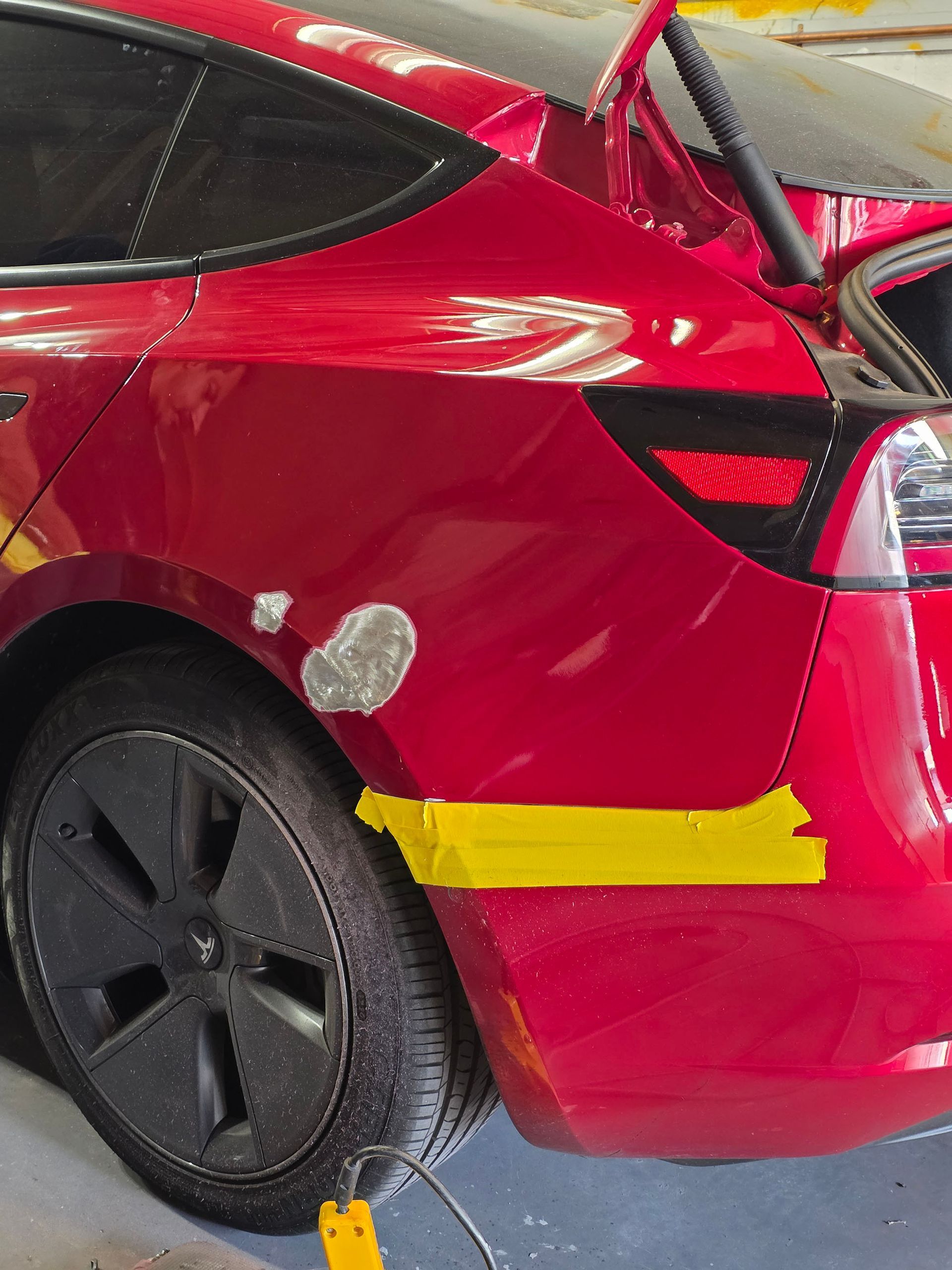 Red car rear side with yellow tape and a damaged wheel arch