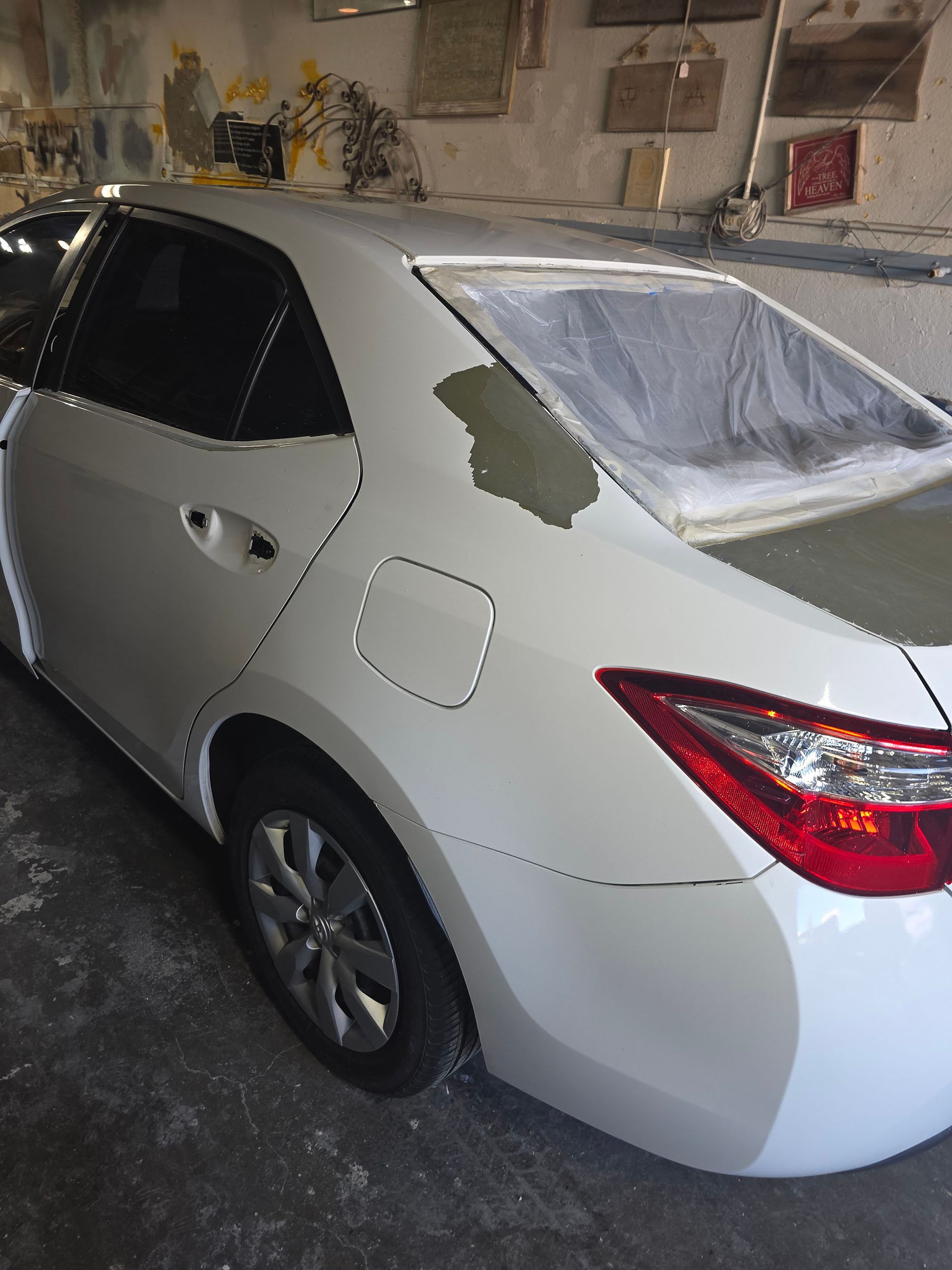 White sedan with fresh gray primer patches on rear quarter panel in a garage