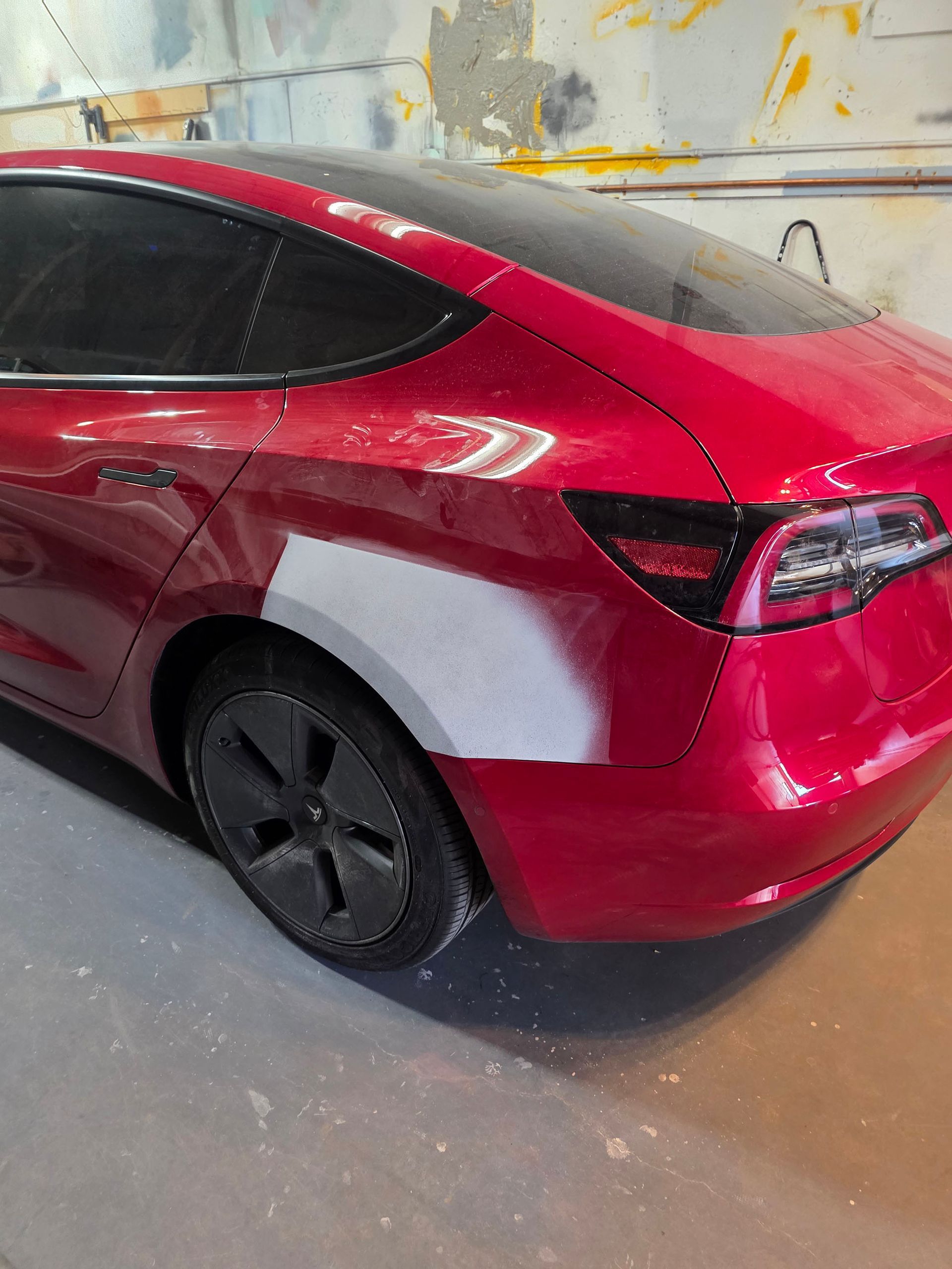 Red sedan with rear quarter panel in primer inside an auto body shop