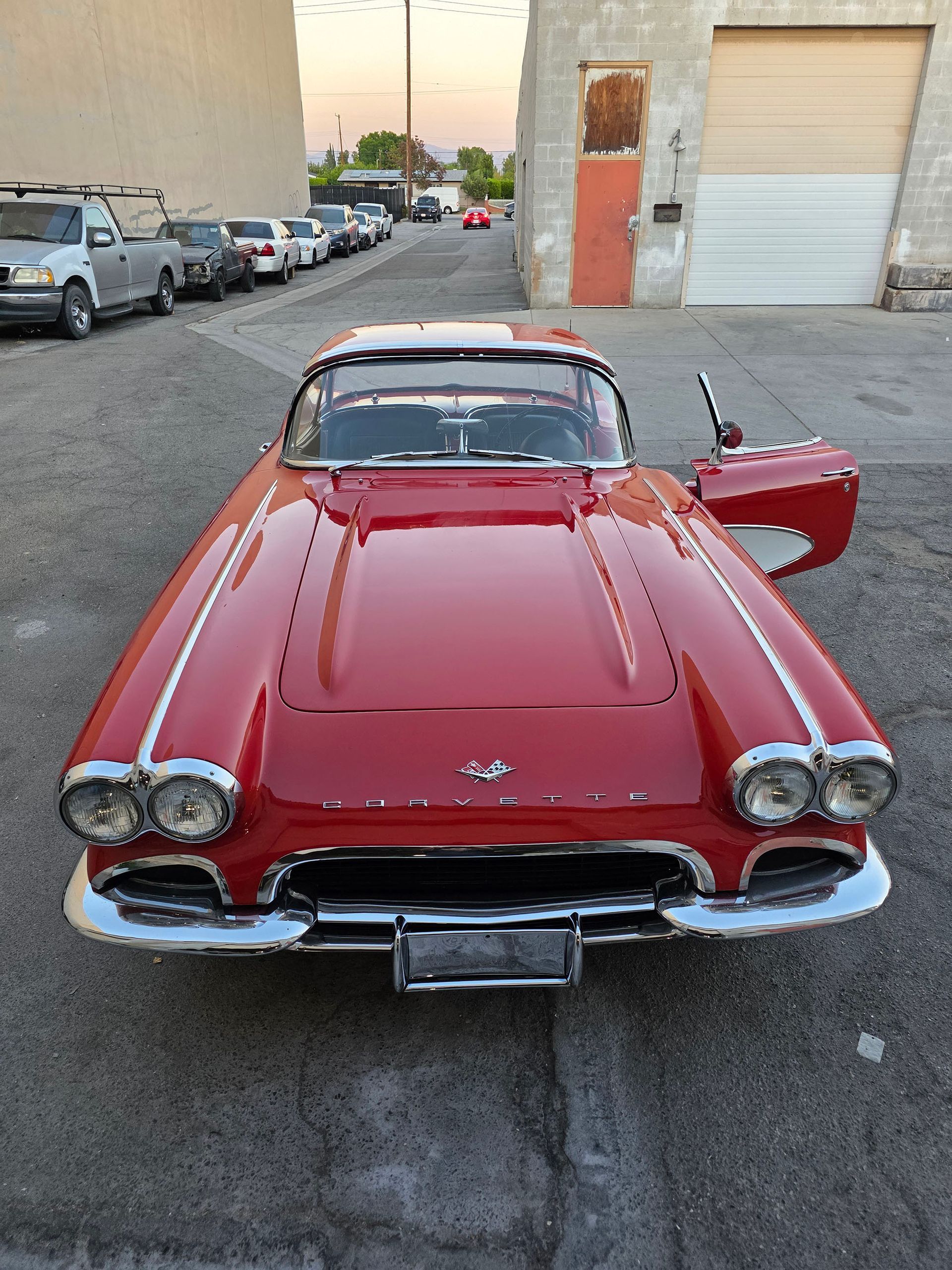 Red classic convertible car parked on an alley, driver’s door open, front view.