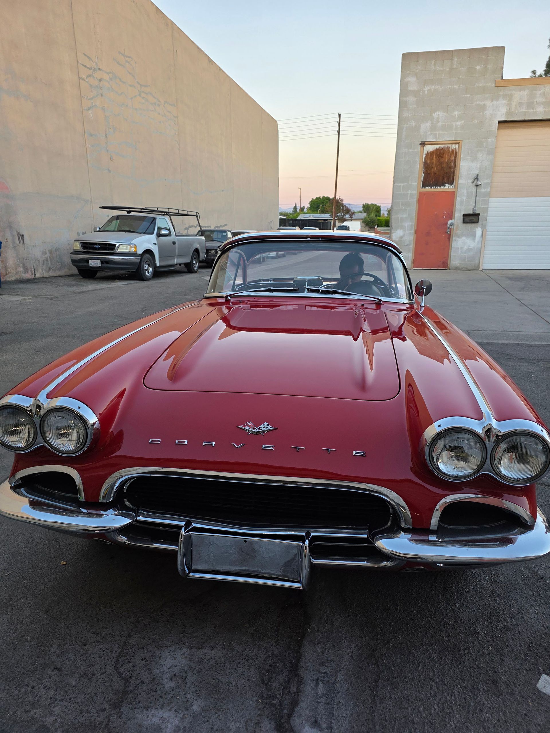 Red classic convertible car parked in an alley, front view with chrome details.