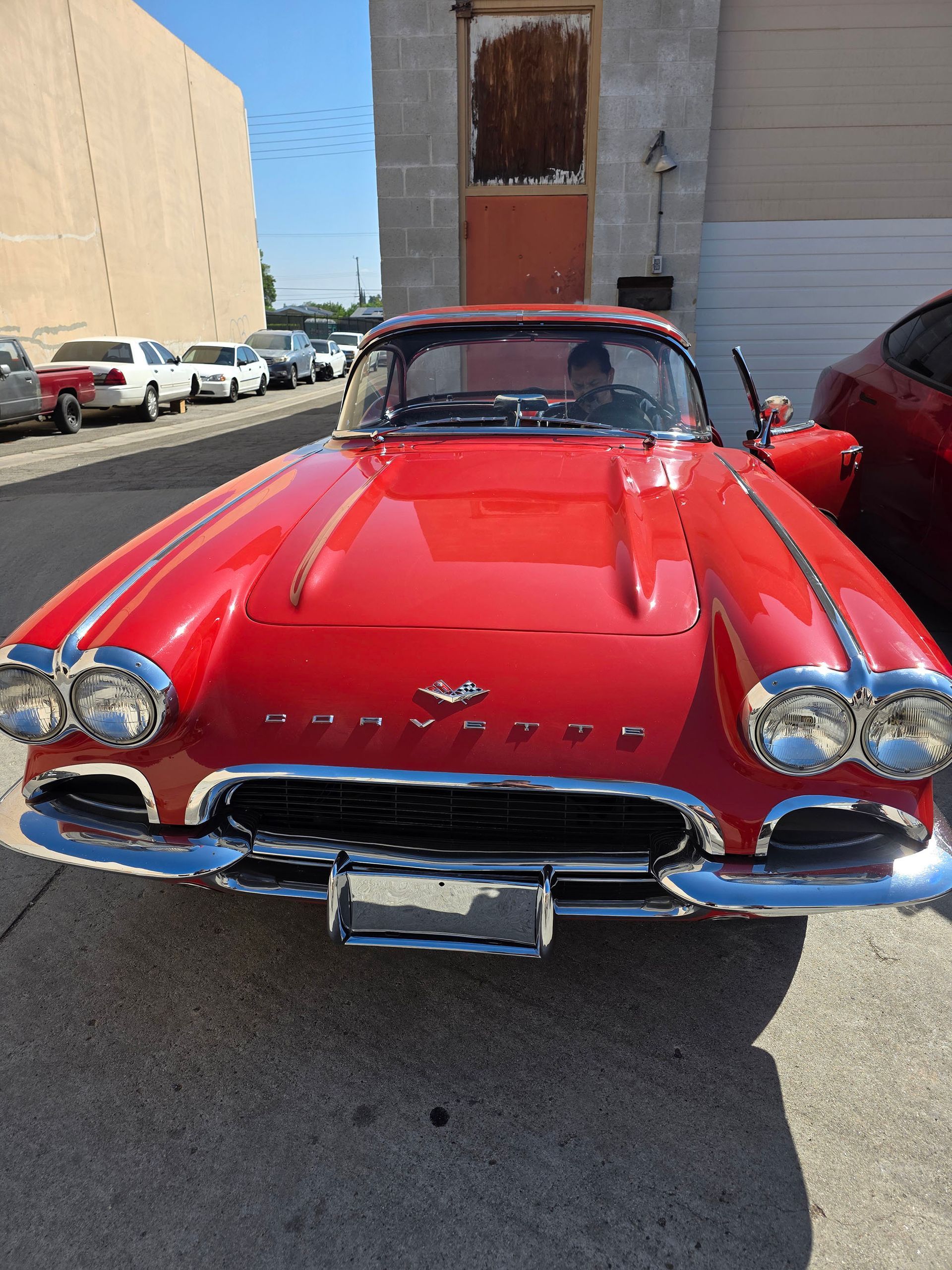 Red classic convertible car parked on a street, front view, with chrome details and a bright red body.