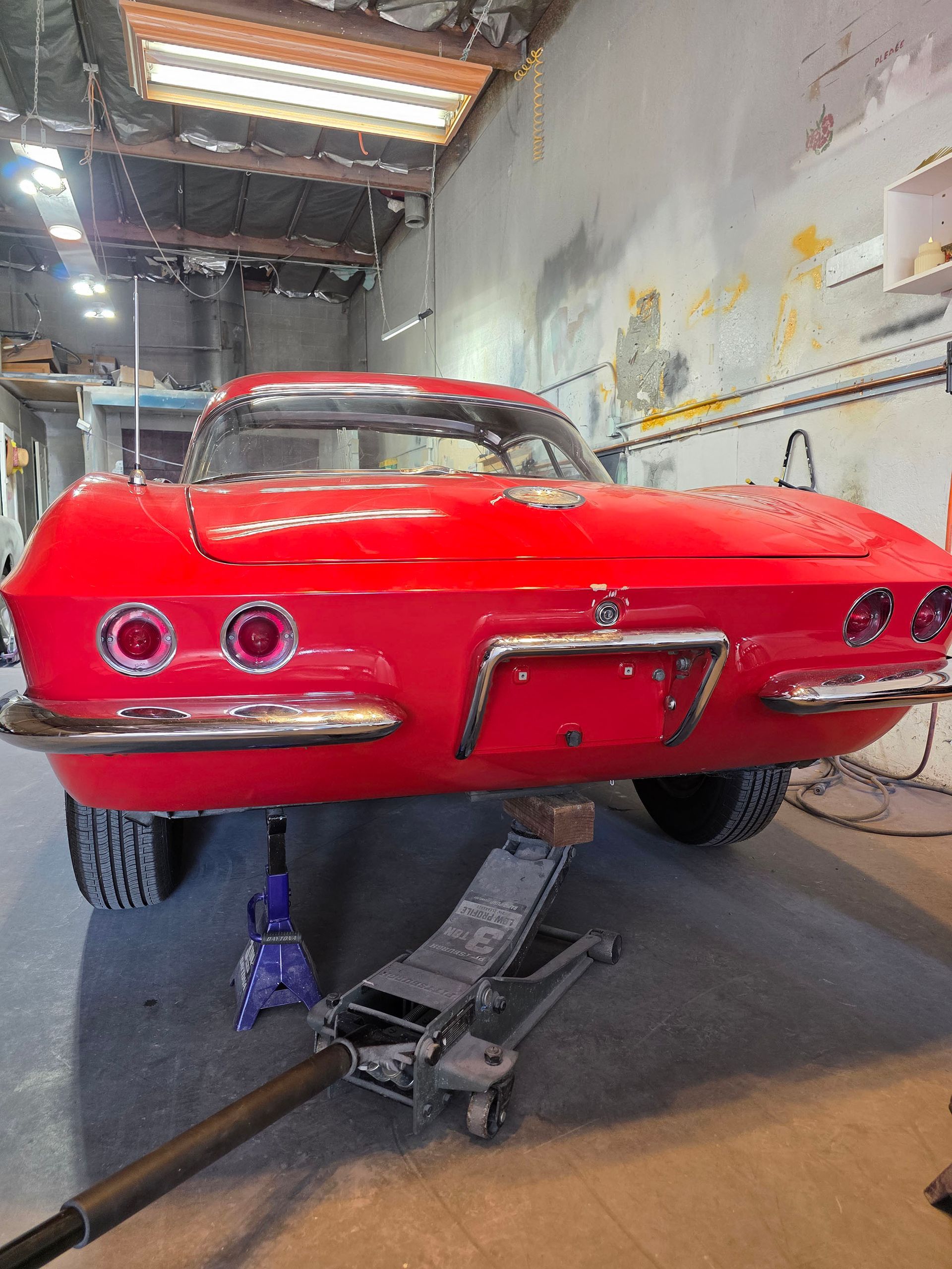 Red classic car lifted on jacks in a workshop, viewed from the rear.