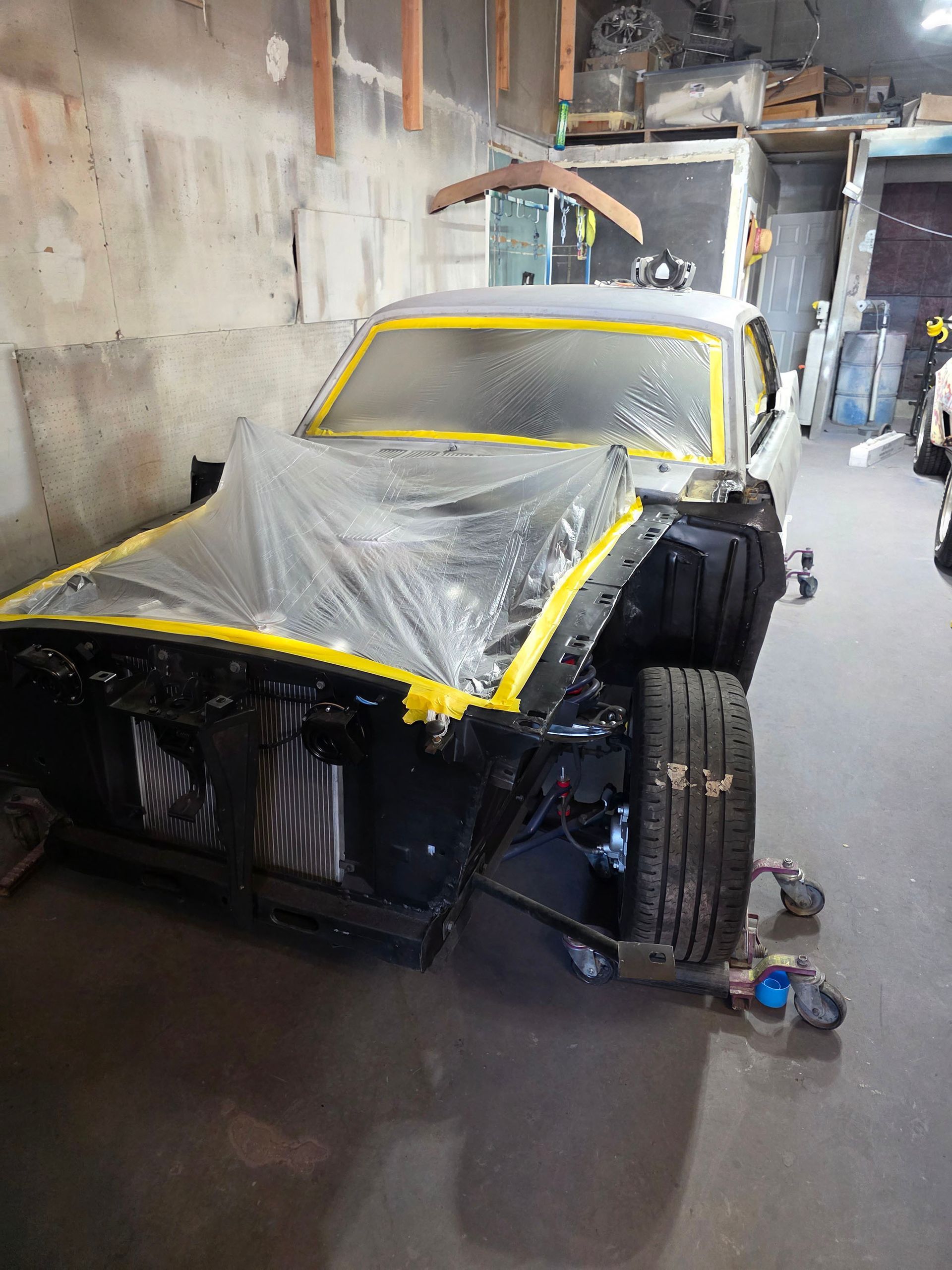 Partially restored car in a workshop, taped and covered in plastic with front body panels removed