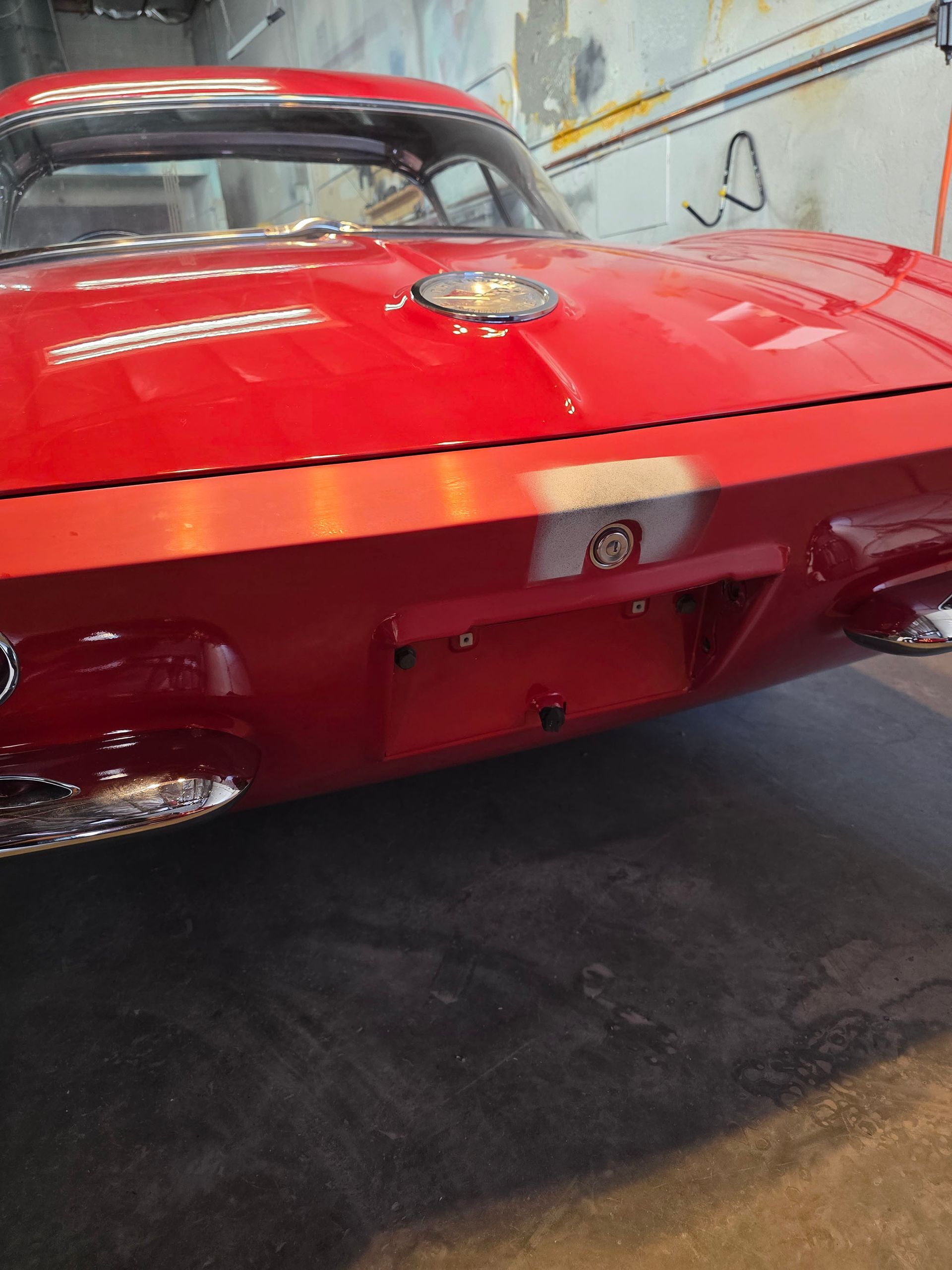 Rear view of a red classic car in a garage, showing chrome bumper and taillights