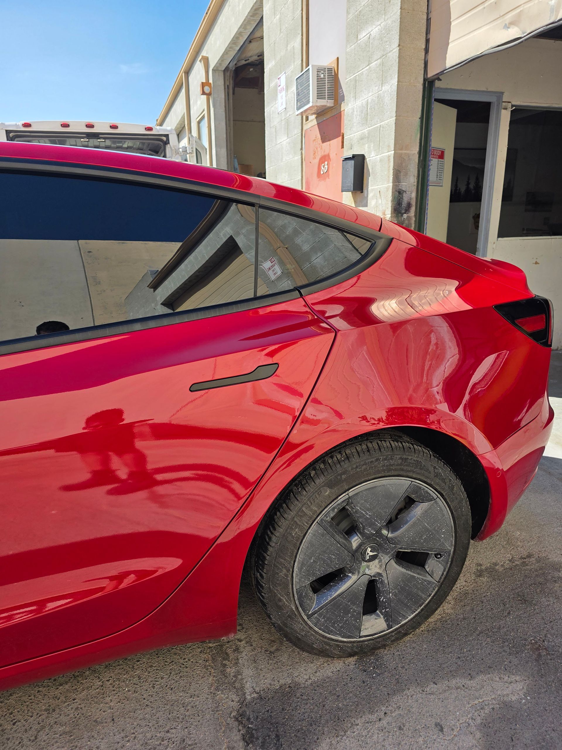 Red sedan parked beside a building, showing the rear side and wheel.