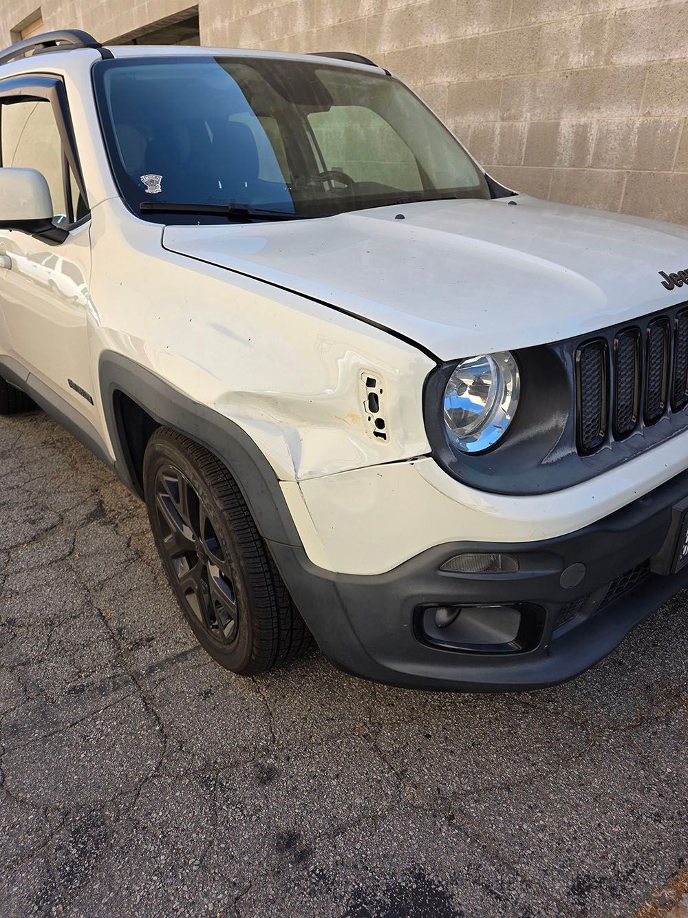 White Jeep Renegade parked beside a concrete wall, front-left view with black trim and wheels