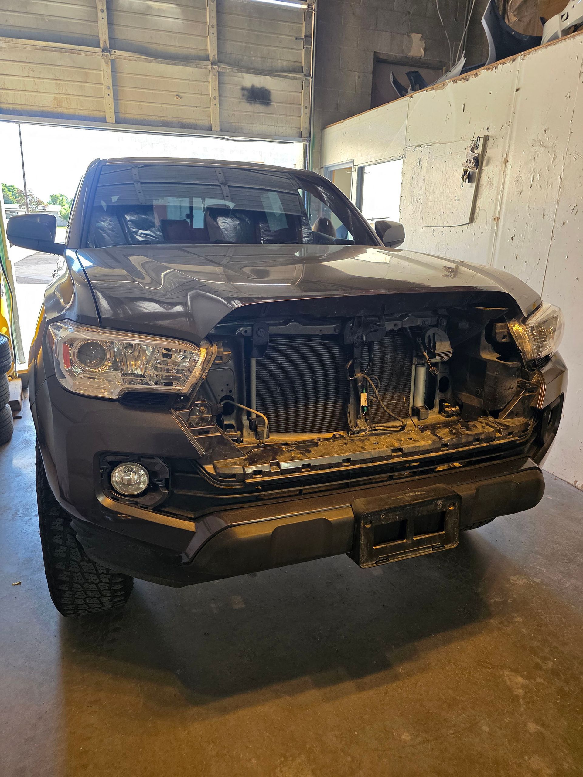 Damaged black pickup truck parked indoors with a smashed front grille and exposed front end