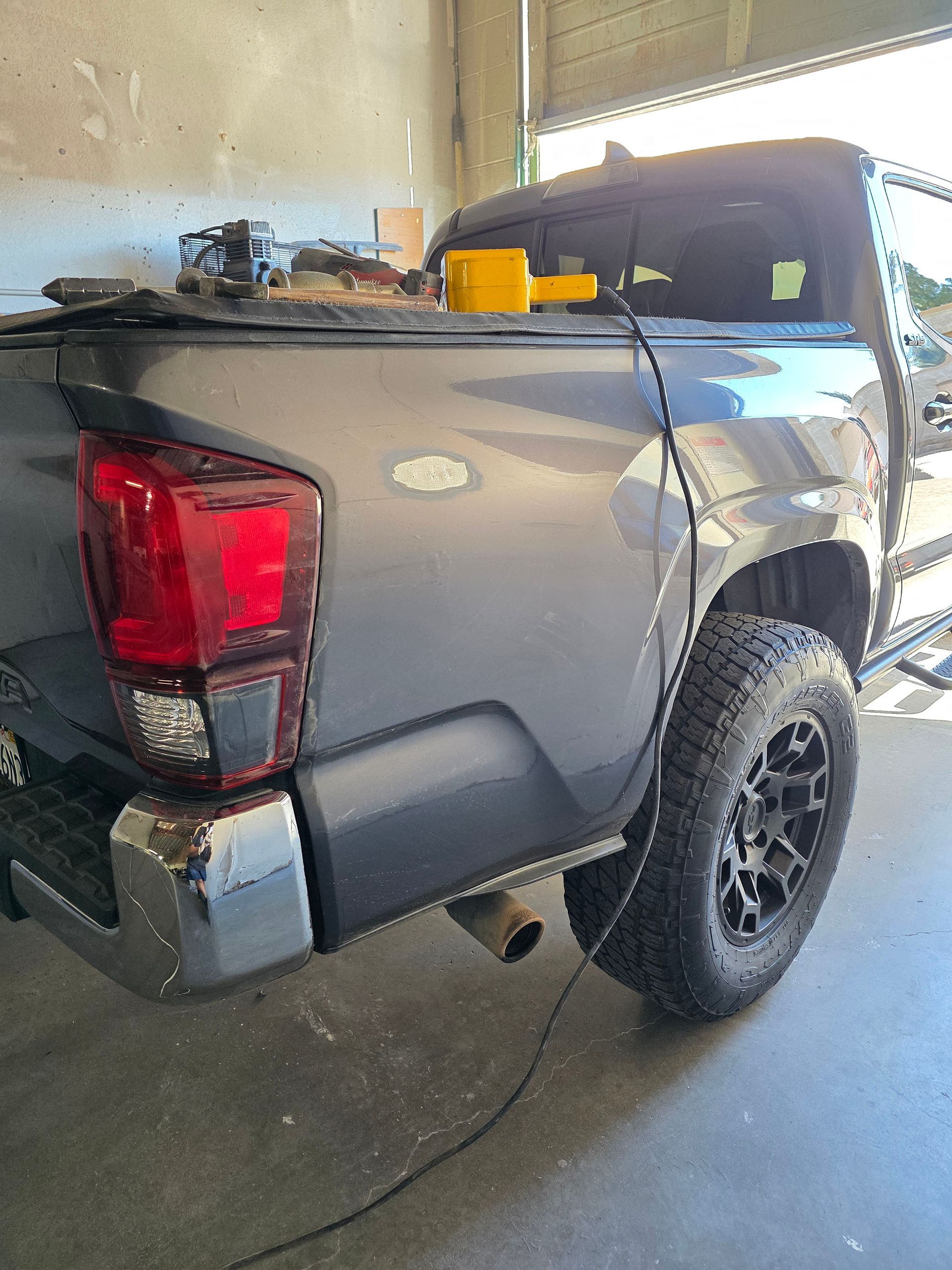Gray pickup truck parked in a garage, rear view with black wheels and a topper on the bed