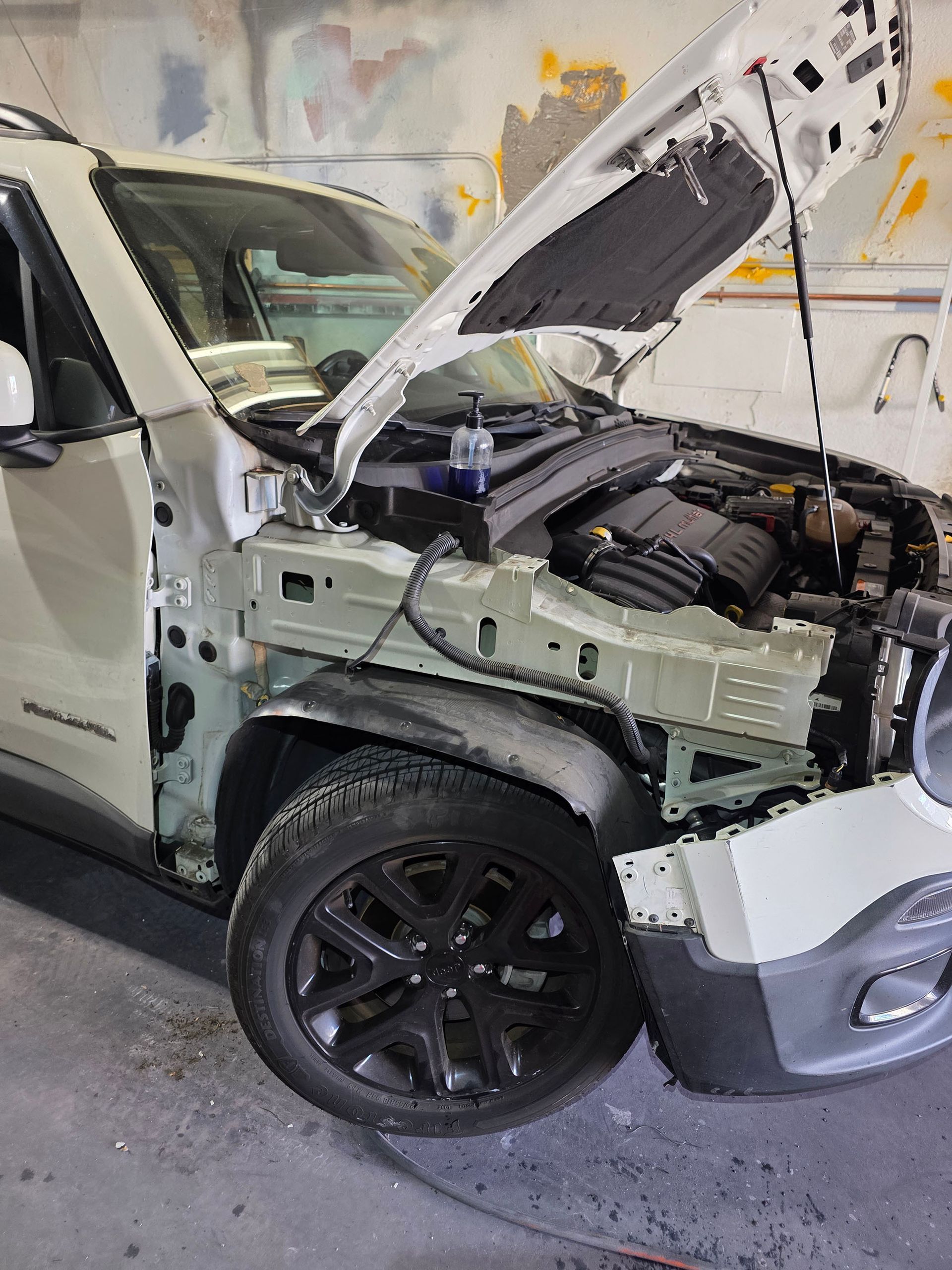White pickup truck with hood open and front body panels removed, showing engine in a garage.