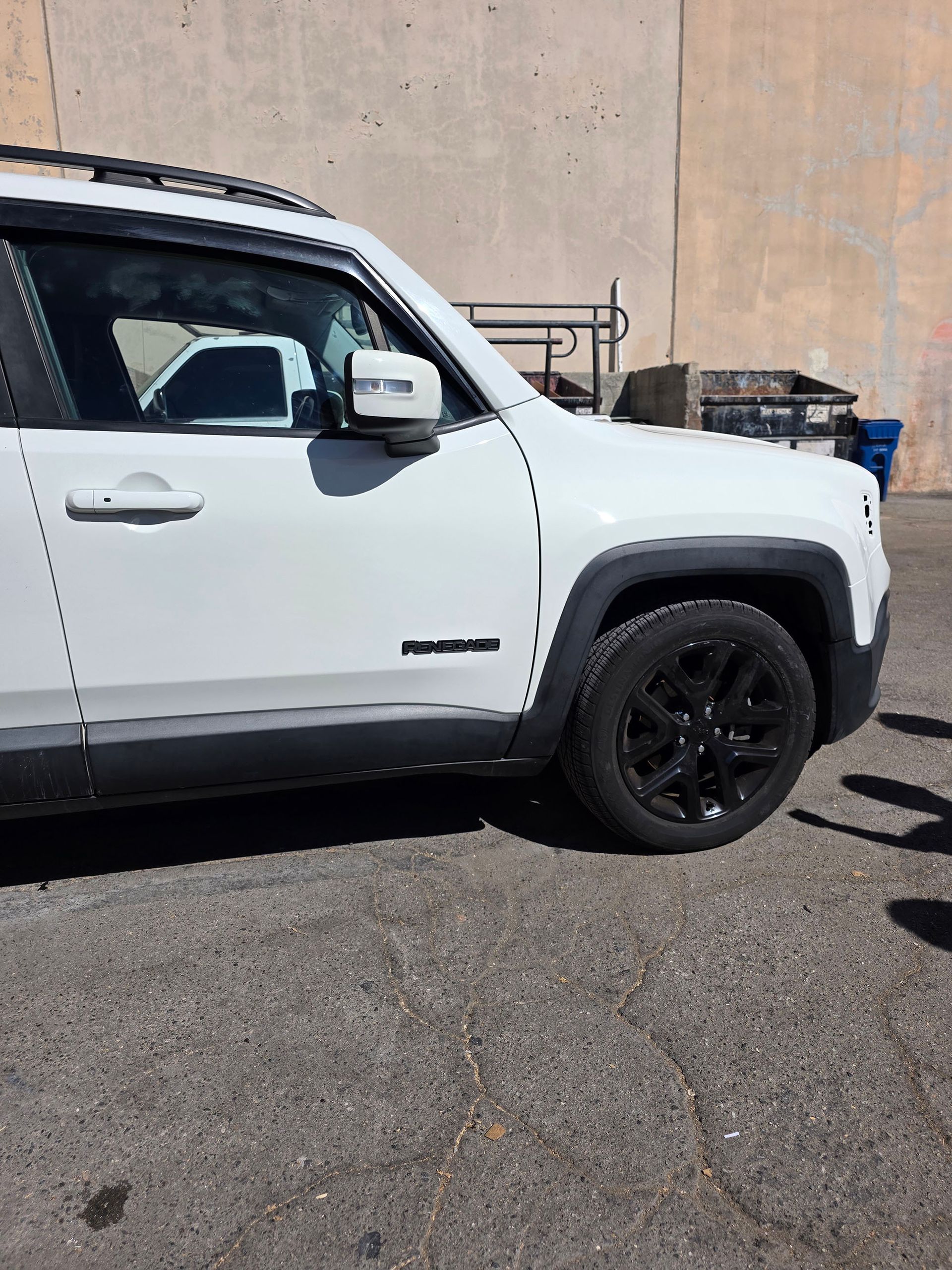 White pickup truck parked on pavement beside a beige wall, side view with black wheels