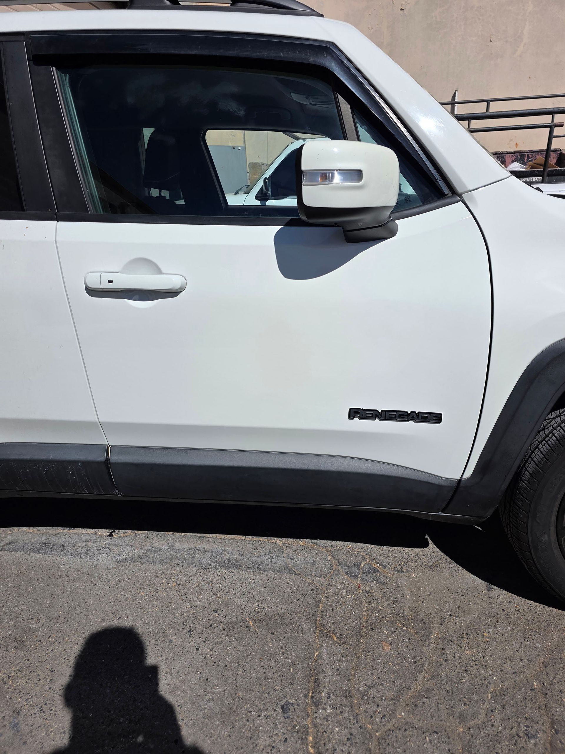 White pickup truck side view parked on pavement, showing the driver door and side mirror.