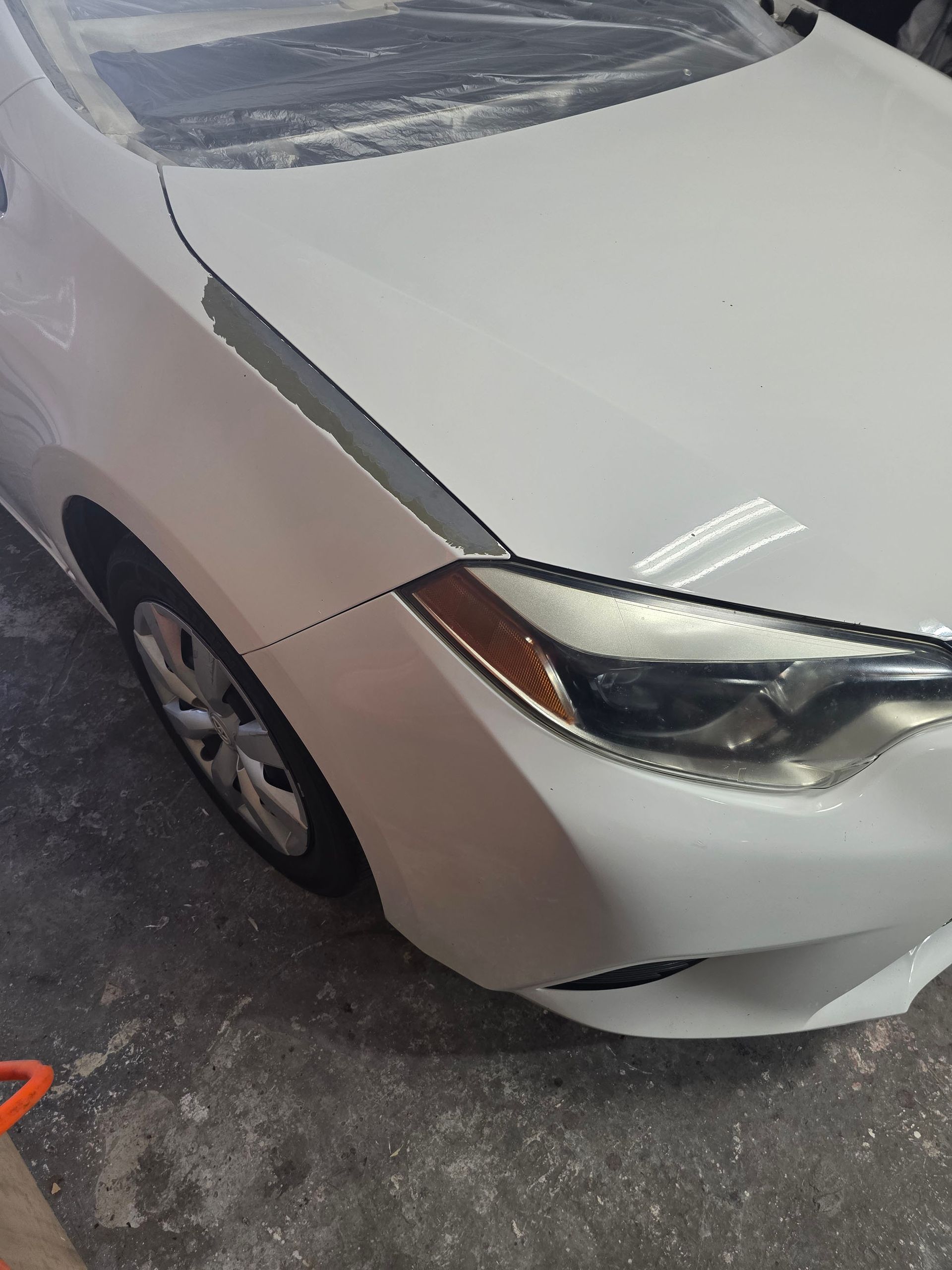 White sedan parked in a driveway, front-right corner visible with minor front bumper damage