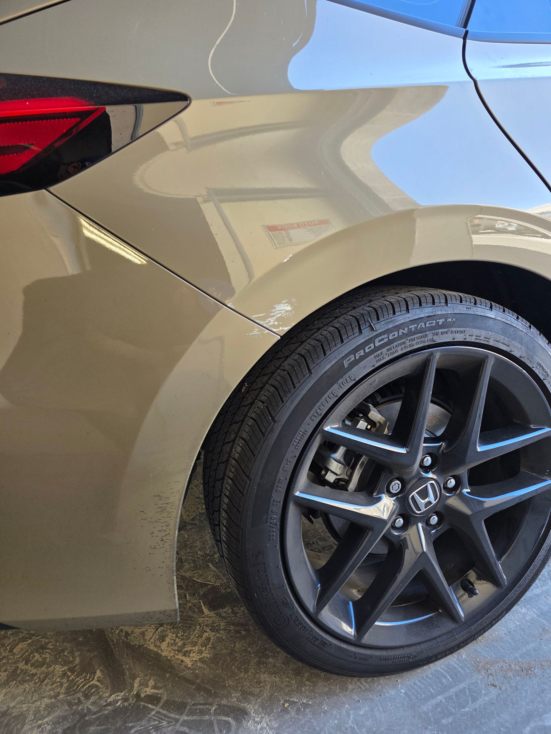 Rear side of a beige car with a black alloy wheel, parked on a driveway.