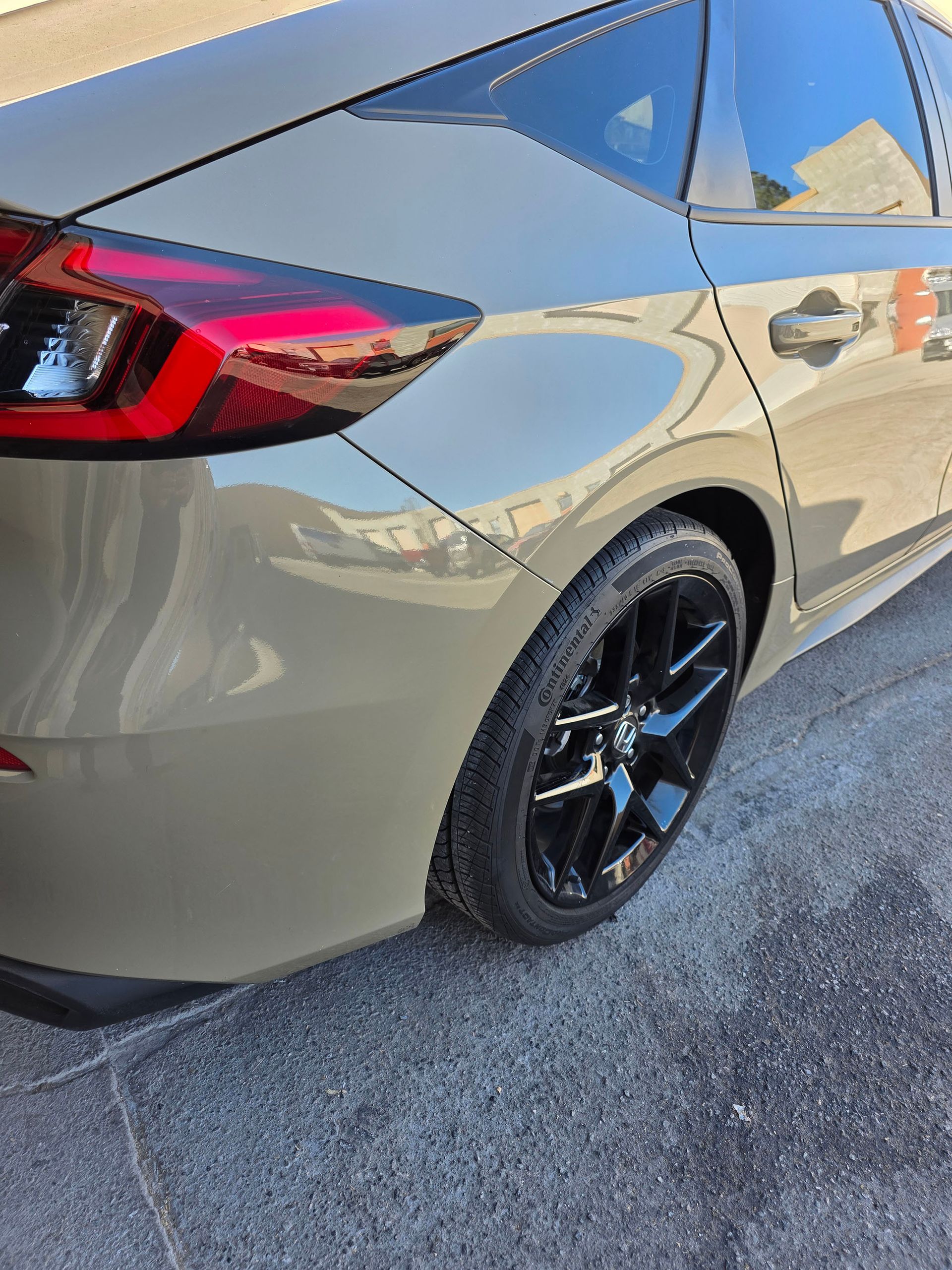 Gray sedan parked outdoors, rear side view with black rims and red taillight accents