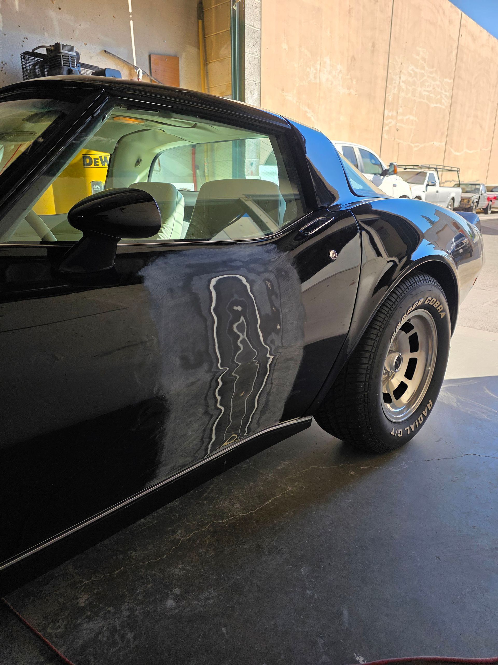 Black sports car with a dented rear side panel parked in a garage area.