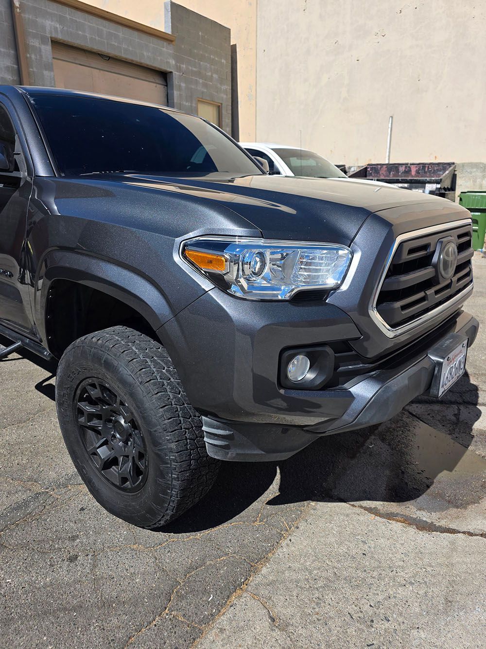 Black Toyota Tacoma pickup truck parked outdoors near a building, front-left view