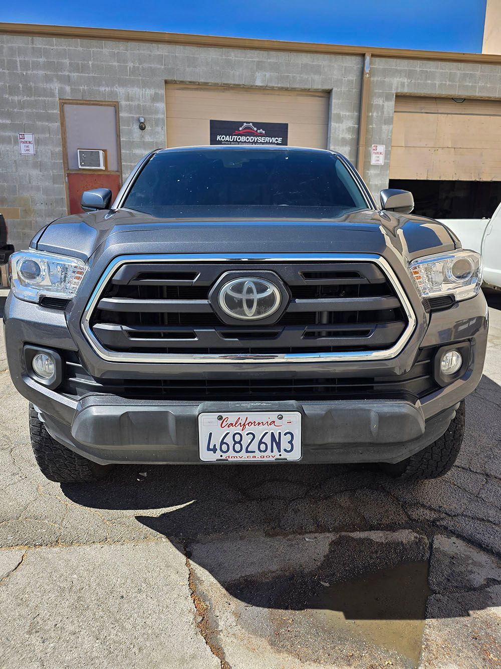 Front view of a gray Toyota pickup parked outside a beige building on a sunny day.