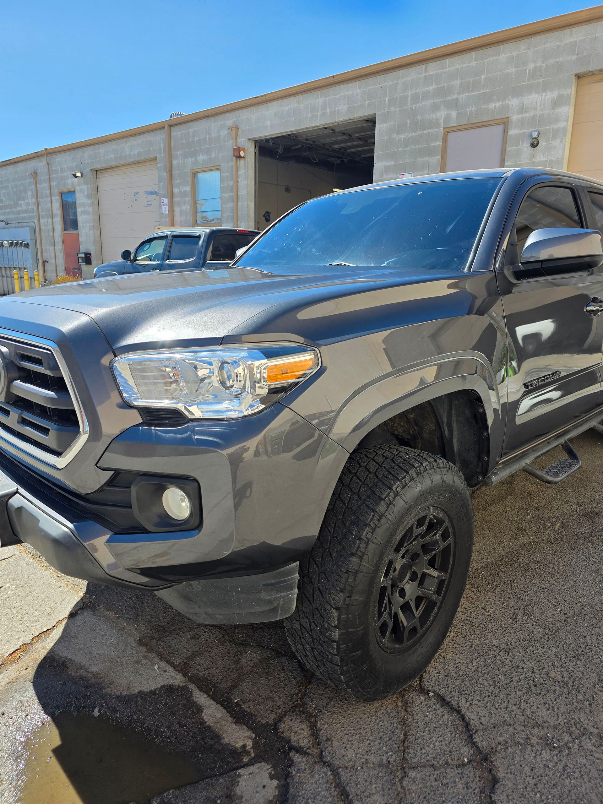 Dark gray pickup truck parked outside an industrial building on a sunny day