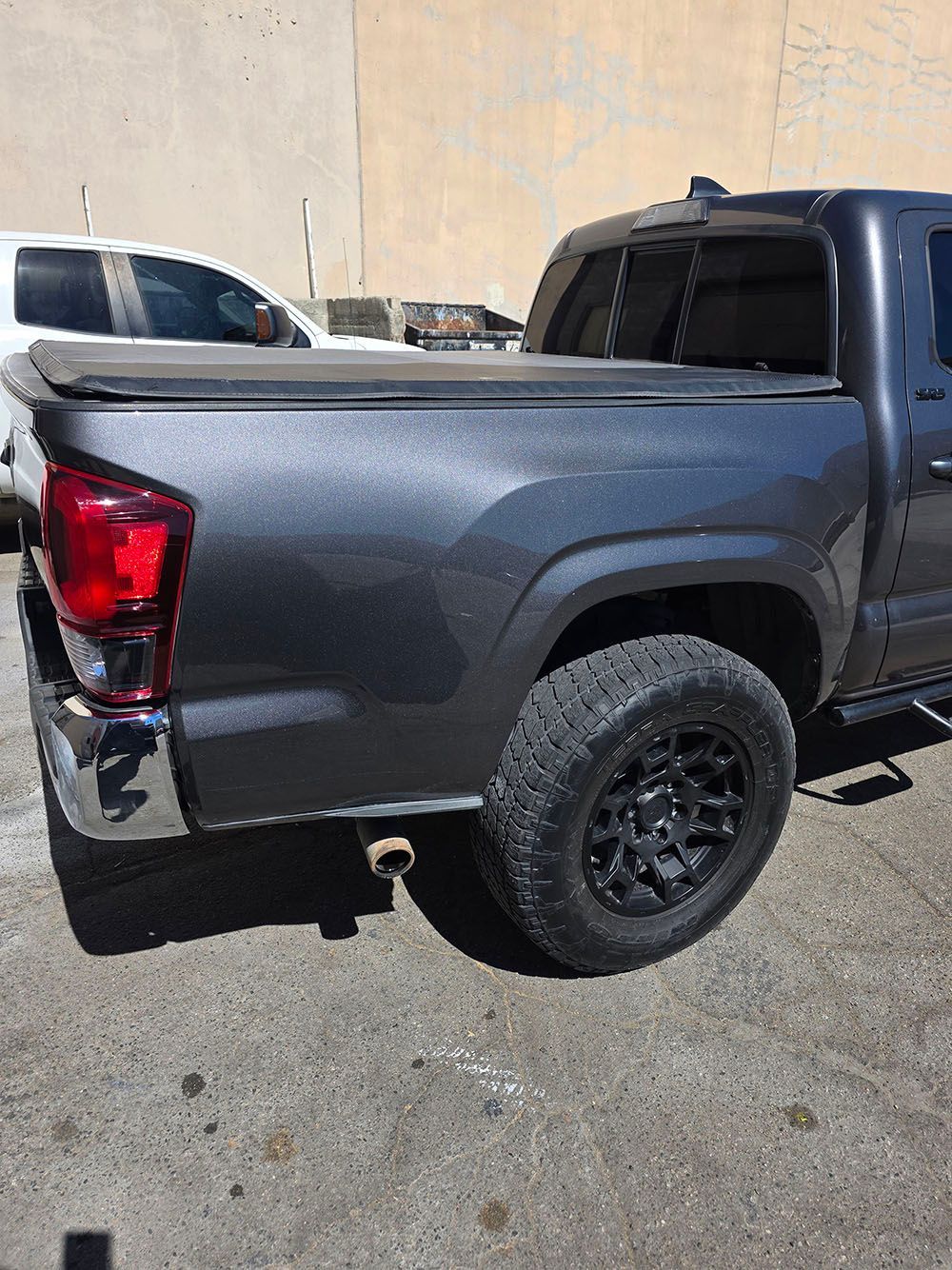 Gray pickup truck parked on pavement, rear side view with black wheels and a red taillight
