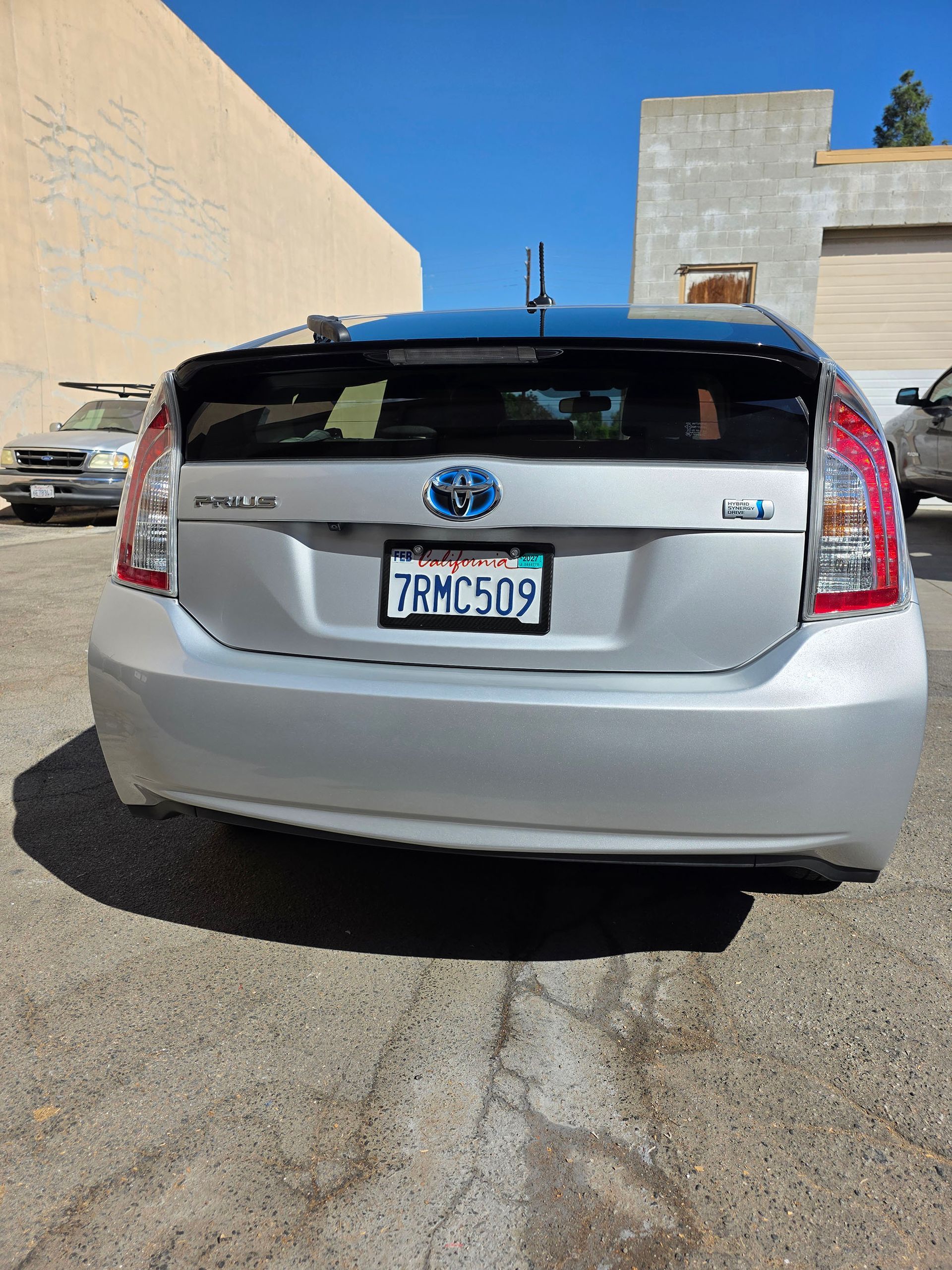 Silver Toyota Prius parked in a lot, rear view with license plate visible under a clear blue sky